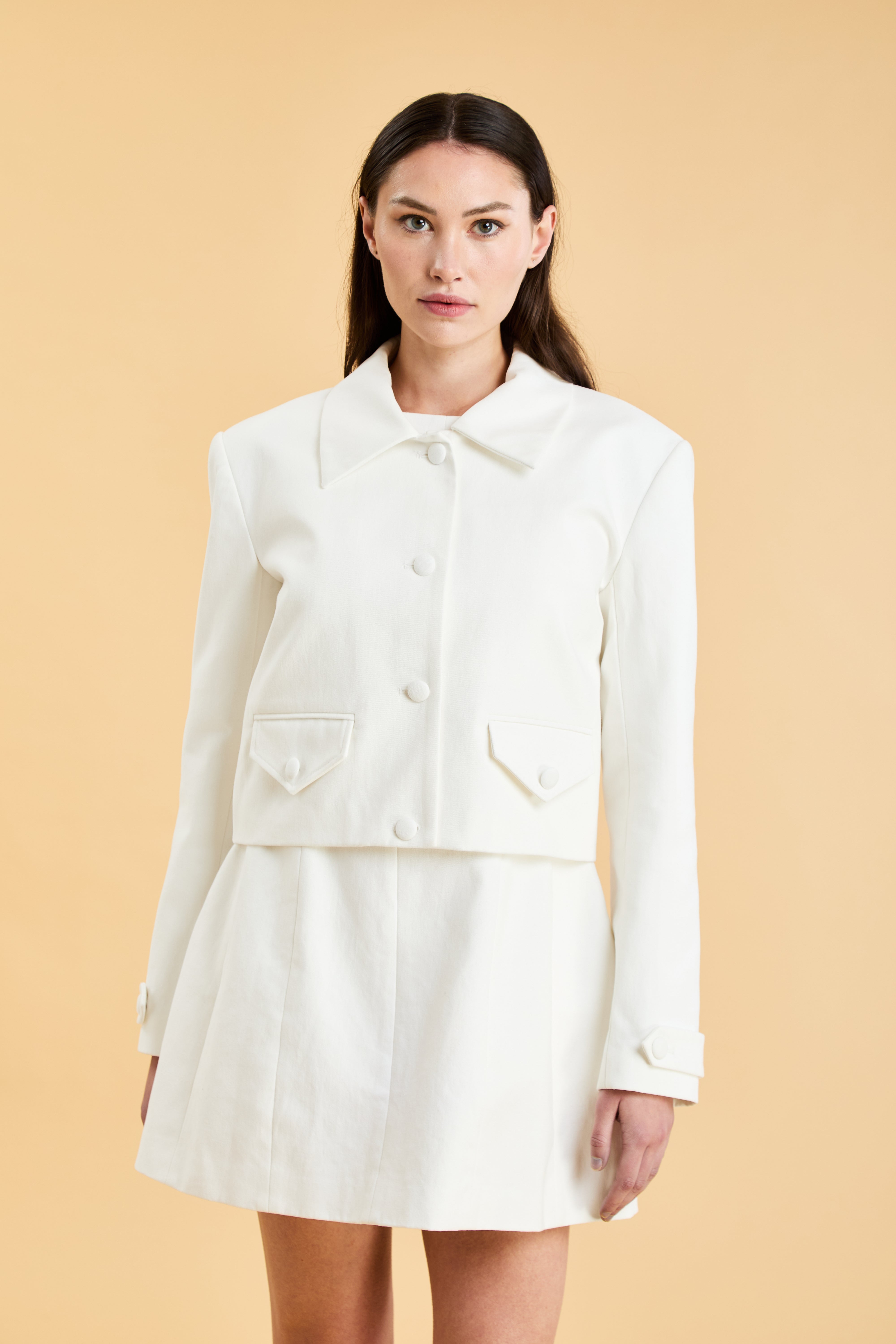 Woman wearing a White Charlotte Jacket and White Louise A-line mini dress on a beige background
