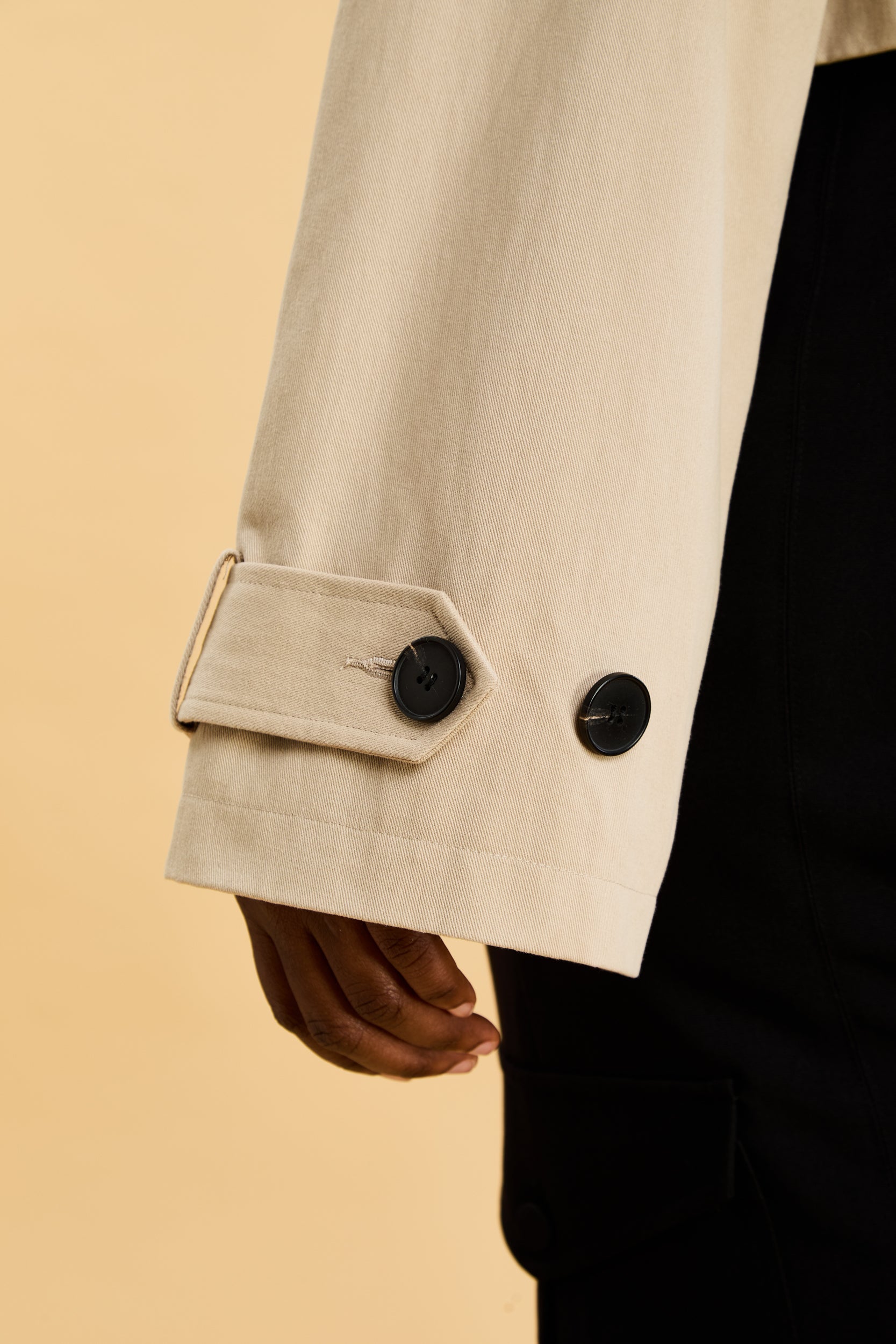 Close-up of a beige coat with black buttons on a beige background
