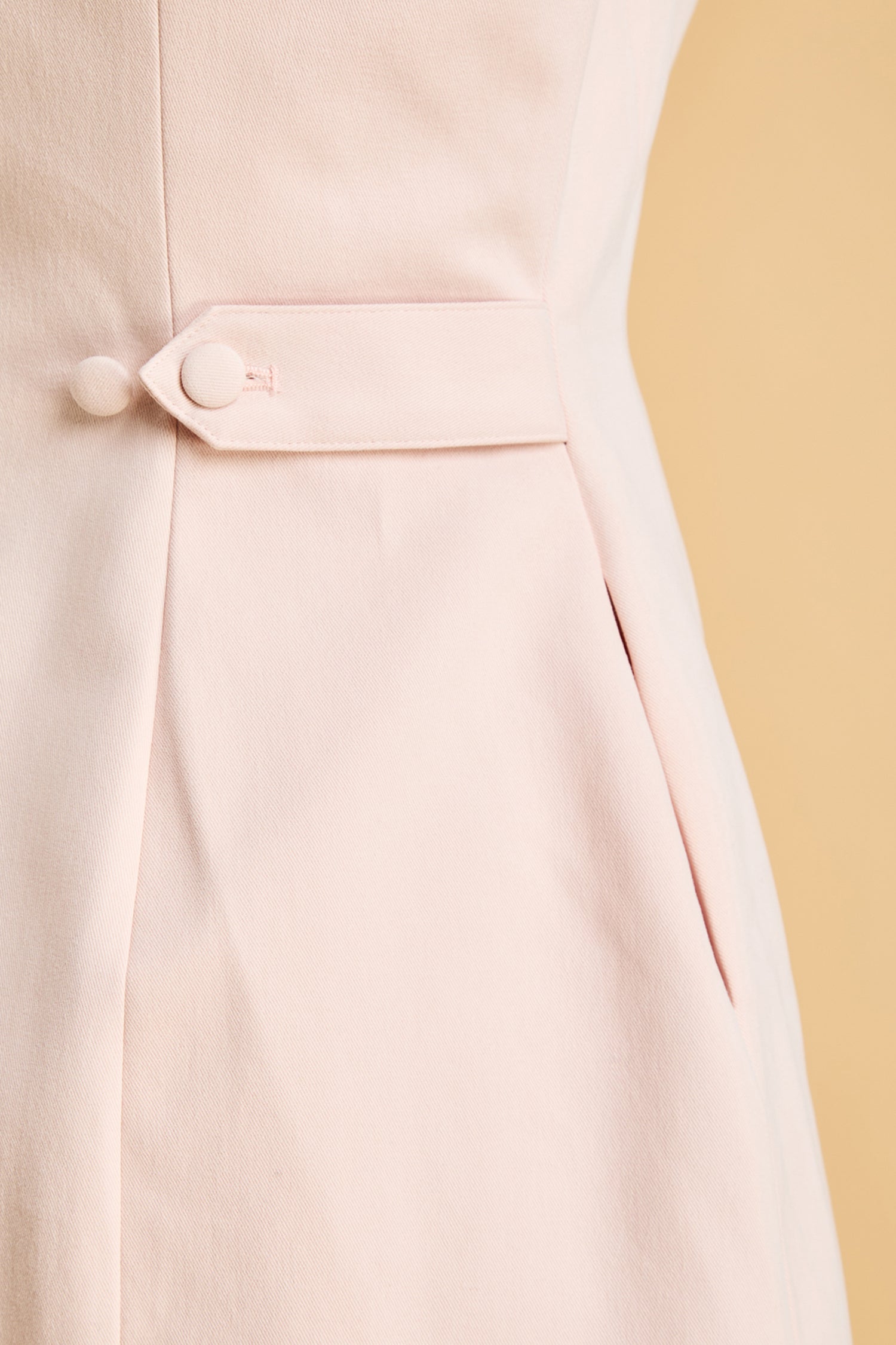 Close-up of a light pink dress with a button detail on a beige background
