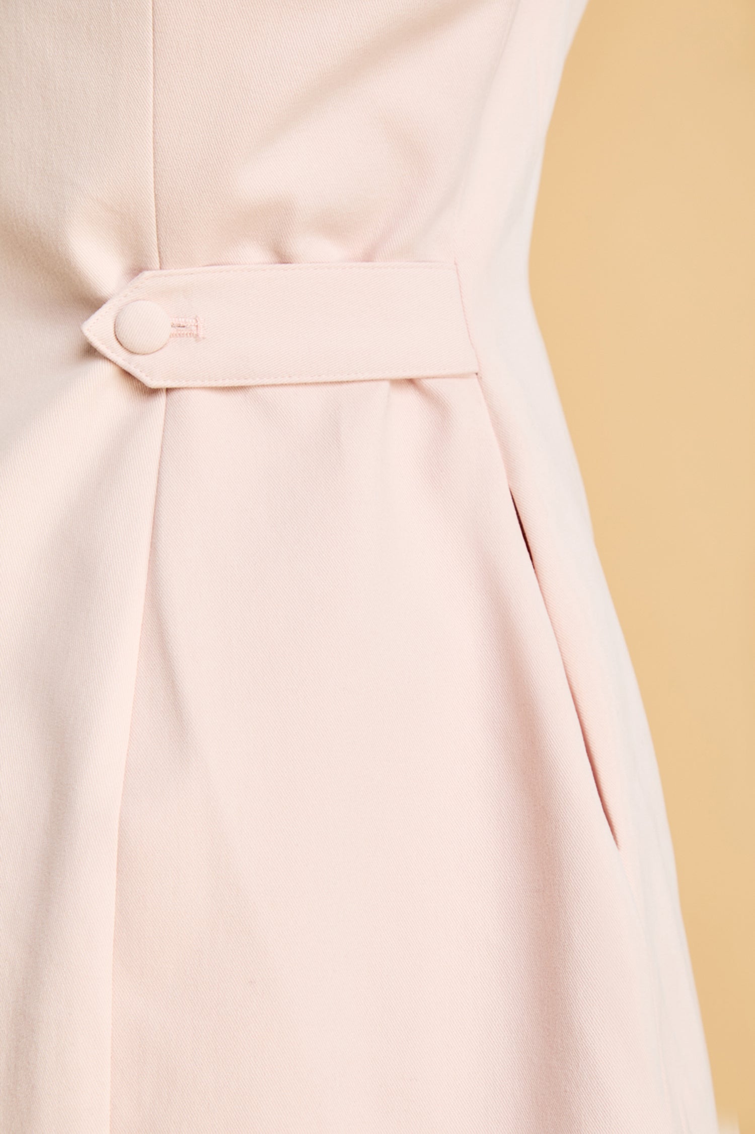 Close-up of a light pink dress with a belt against a beige background