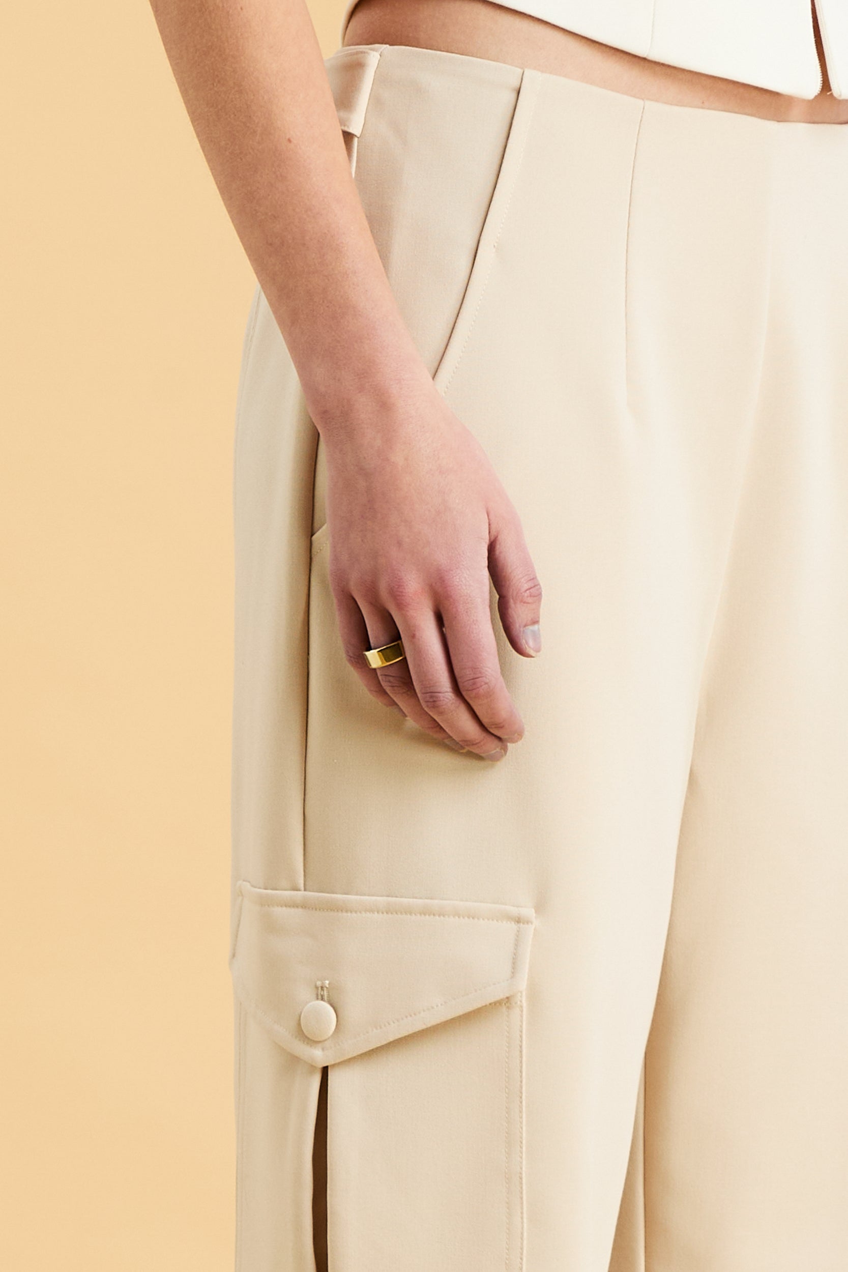 Woman wearing a white sleeveless double zipper top and beige almond Triplicity trousers cargo pants on a beige background