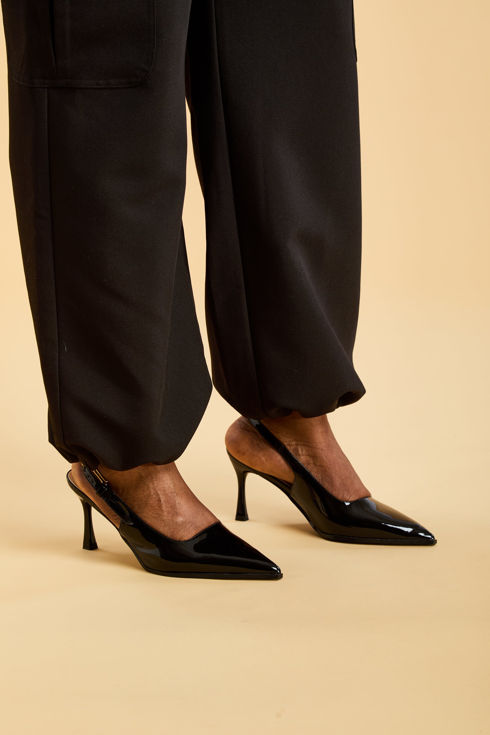 Black high-heeled shoes worn with black pants with drawstring tightened on a beige background