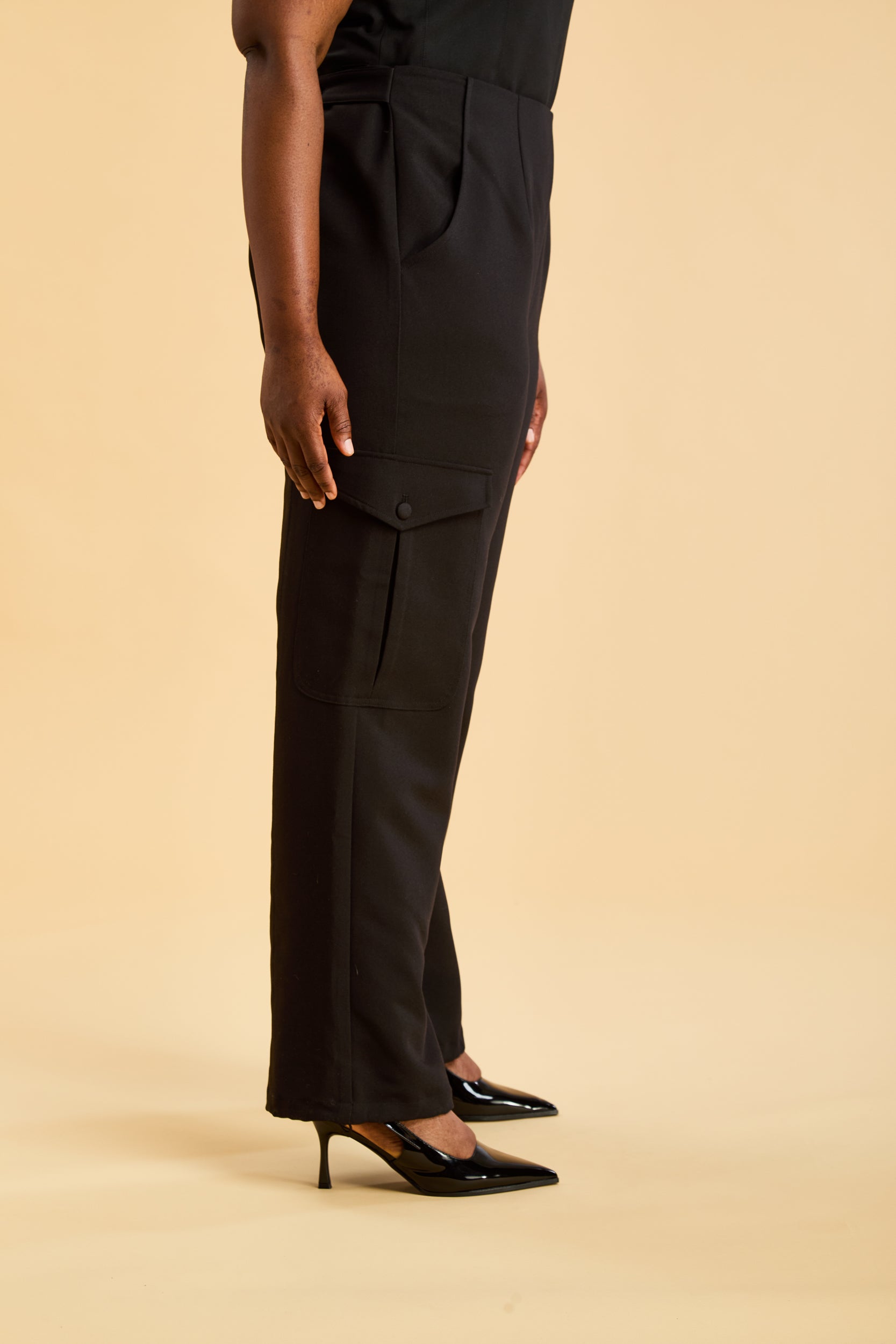 Person wearing a black outfit with high-waisted pants on a beige background