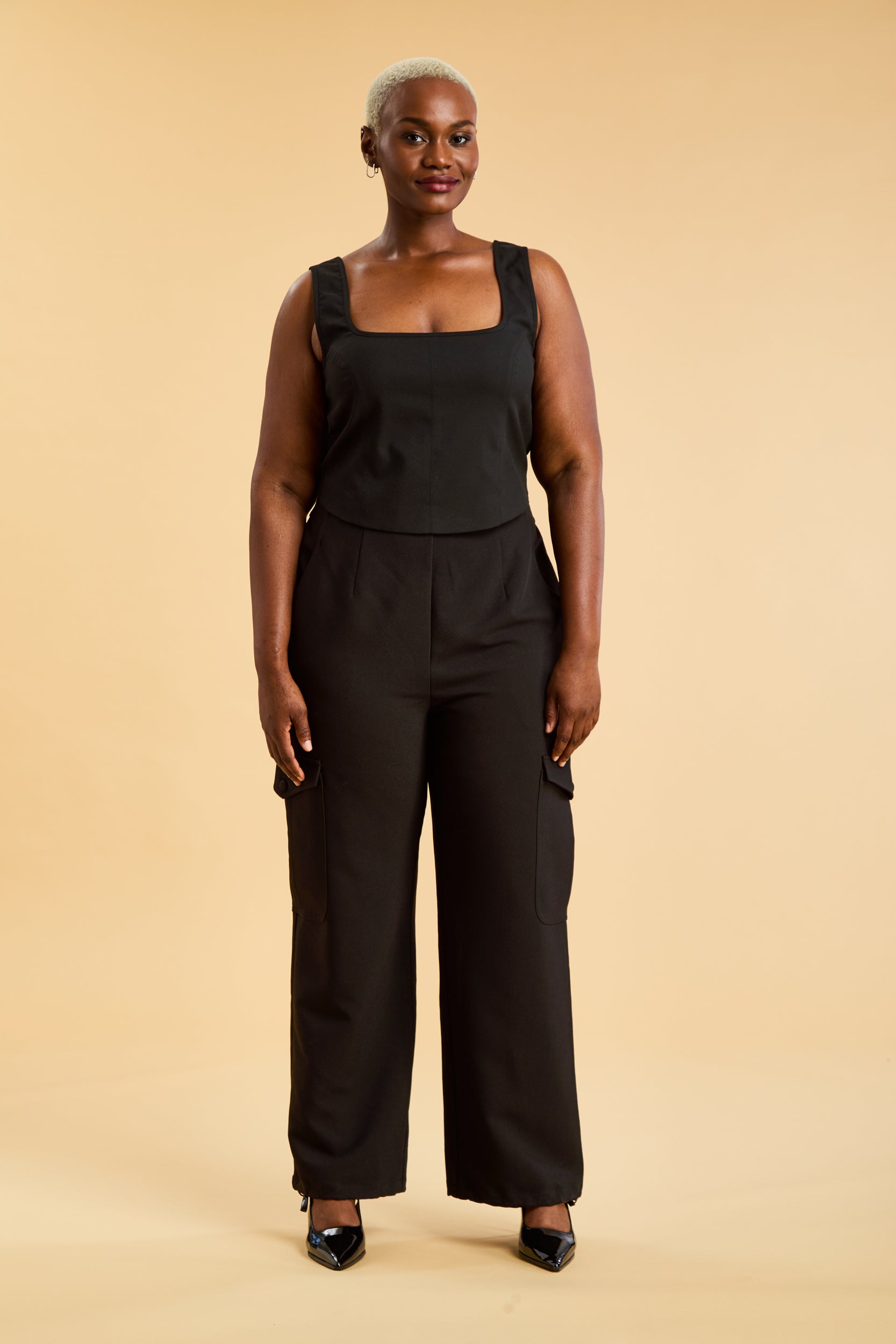 Woman wearing a black top and black cargo pants on a beige background