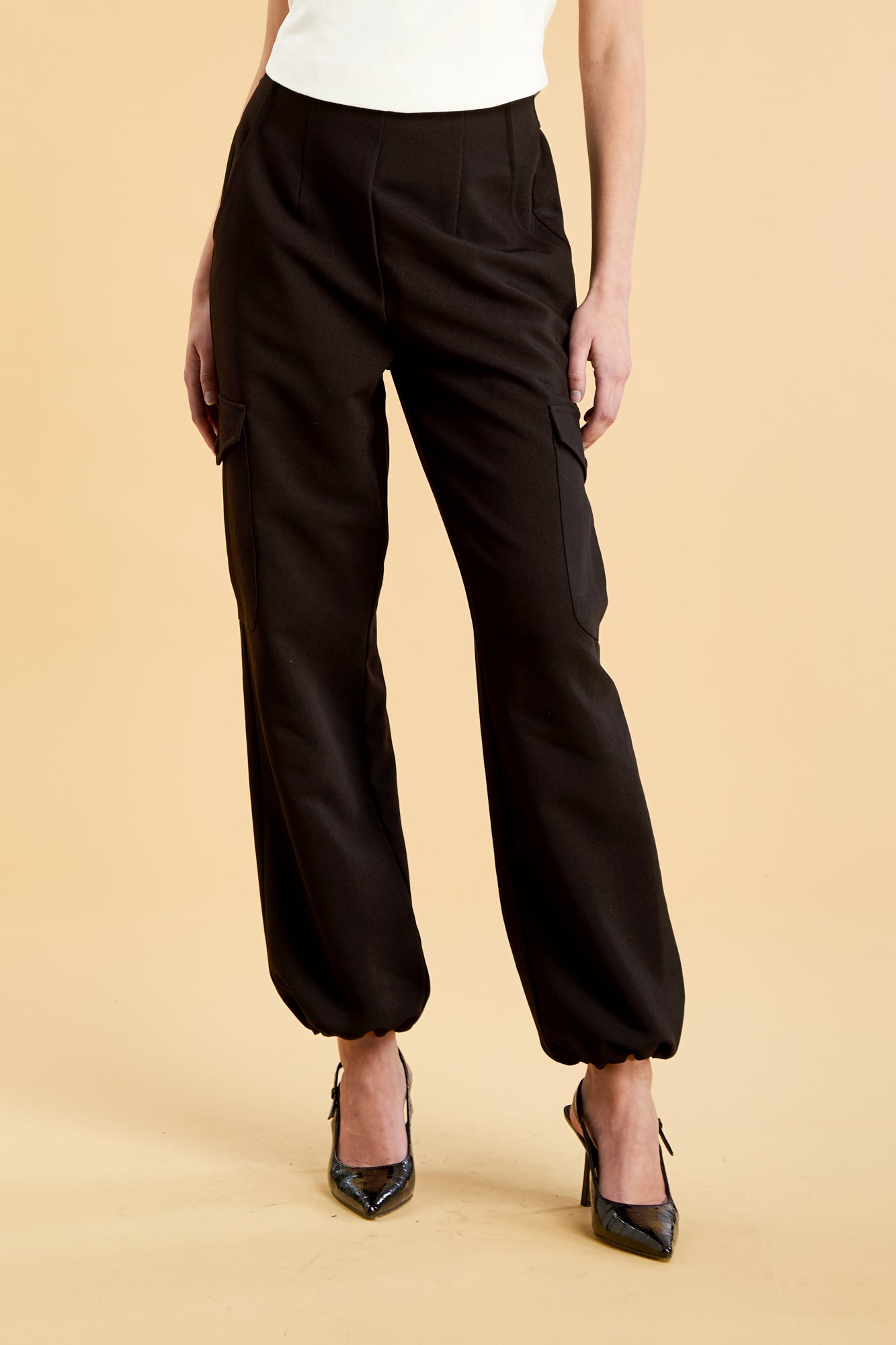 Woman wearing a white top and black cargo pants on a beige background