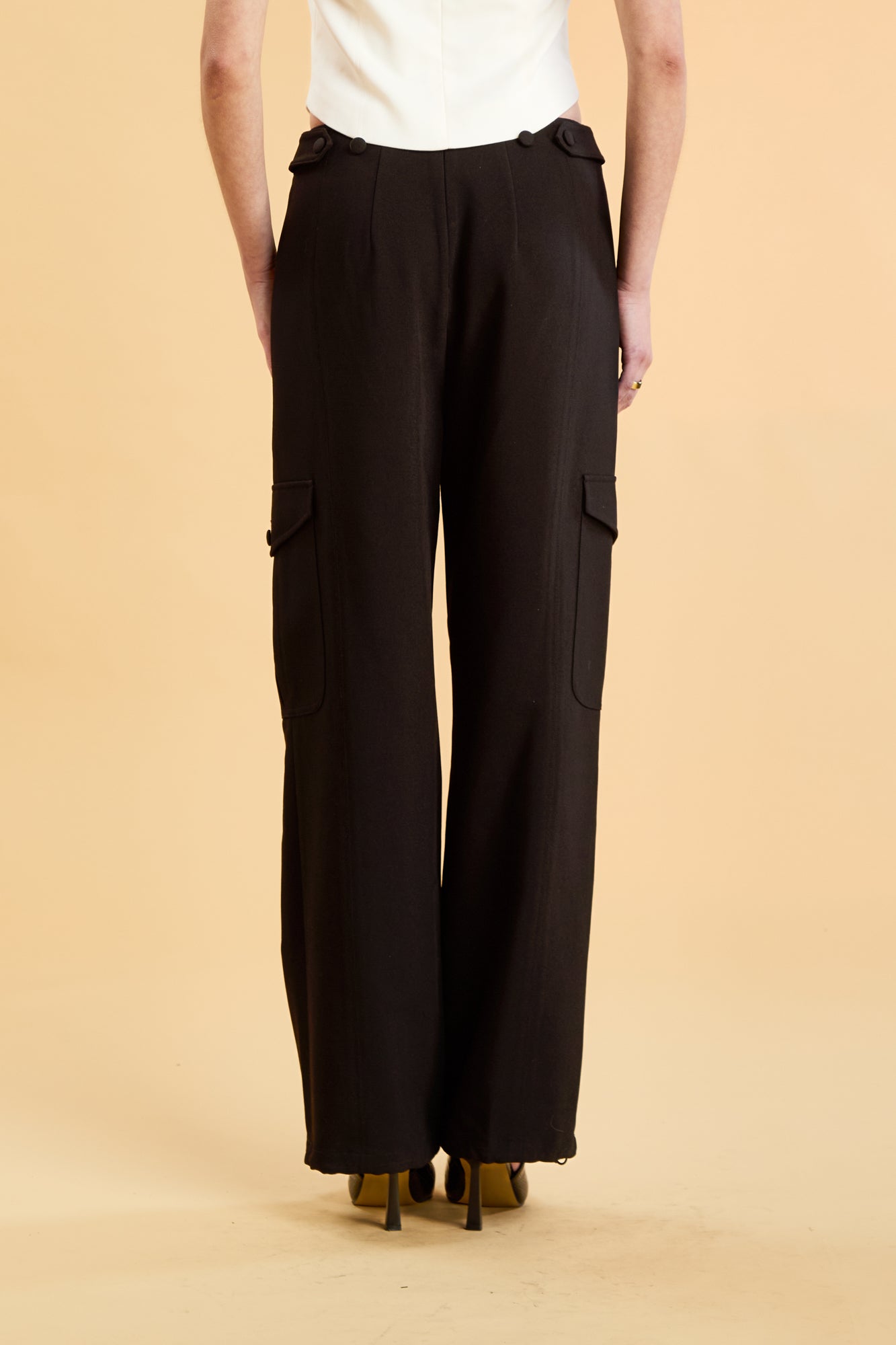 Woman wearing a white top and black cargo pants on a beige background