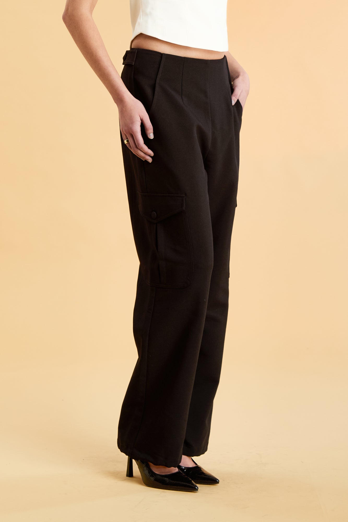 Woman wearing a white top and black cargo pants on a beige background