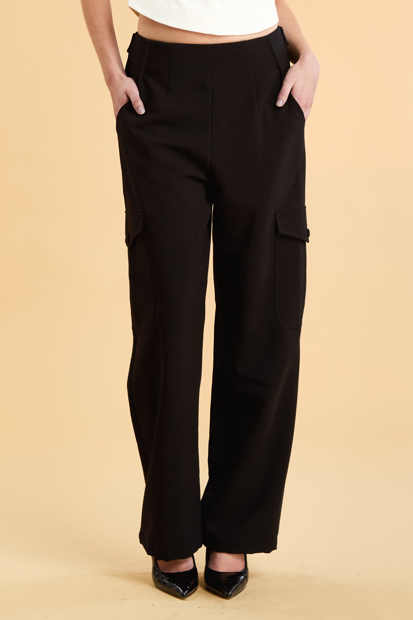 Woman wearing a white top and black cargo pants on a beige background