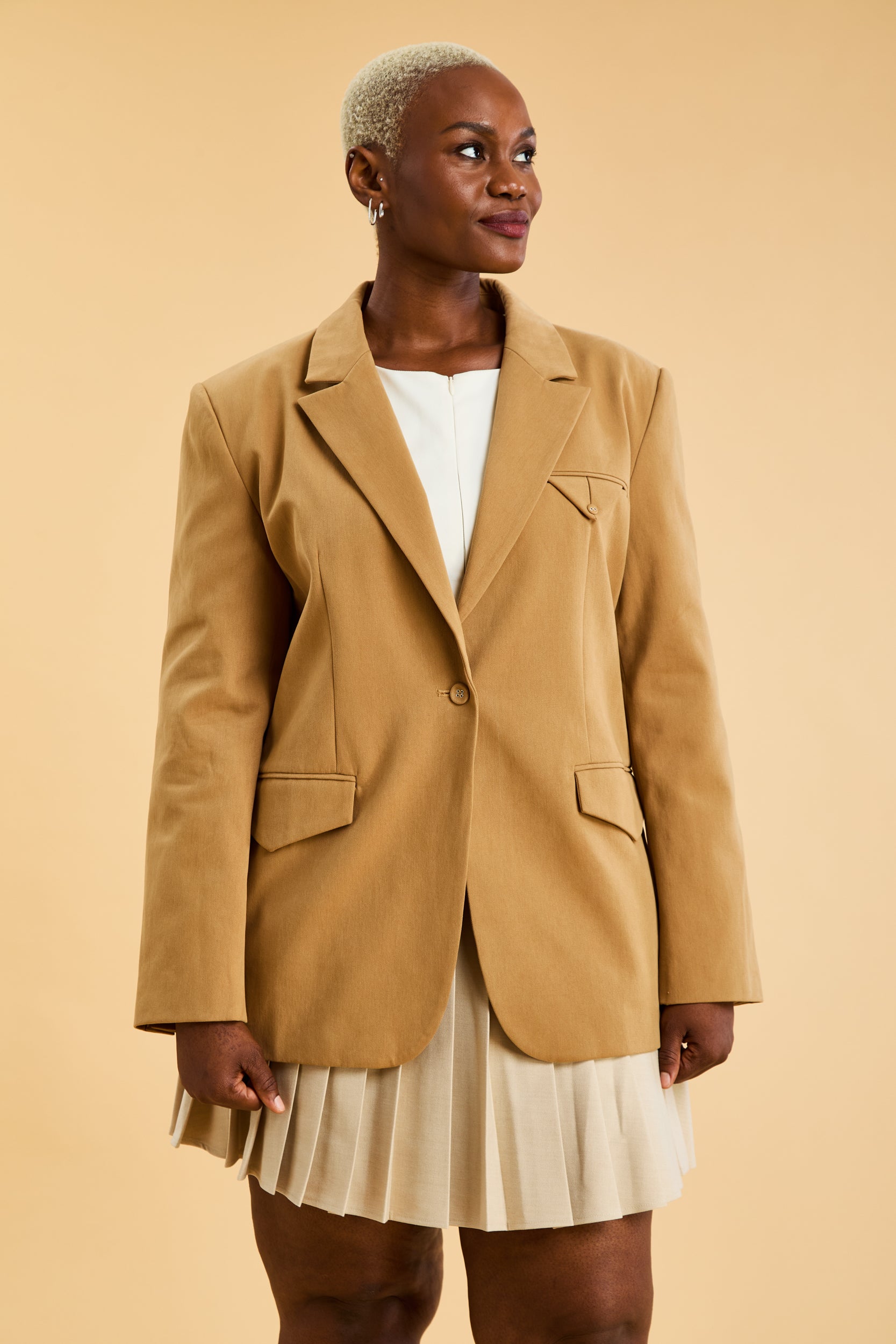 Woman wearing a Camel colored blazer over a white dress on a beige background