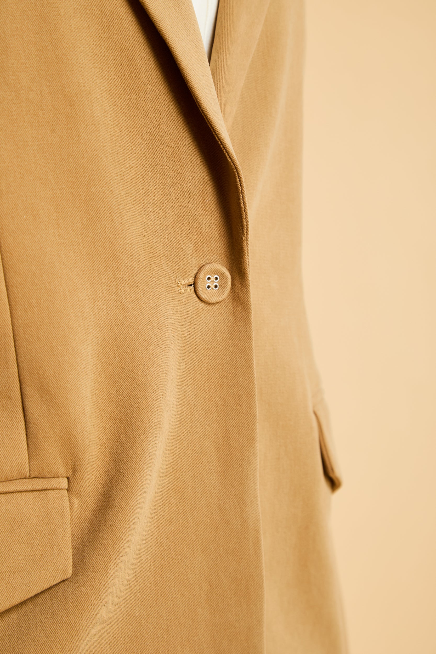 Close-up of a Camel colored coat with a front button on a beige background