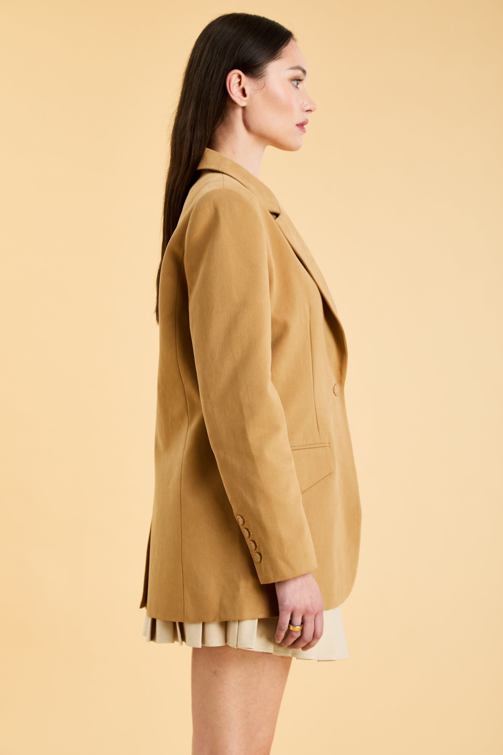 Woman wearing a Camel colored blazer against a beige background
