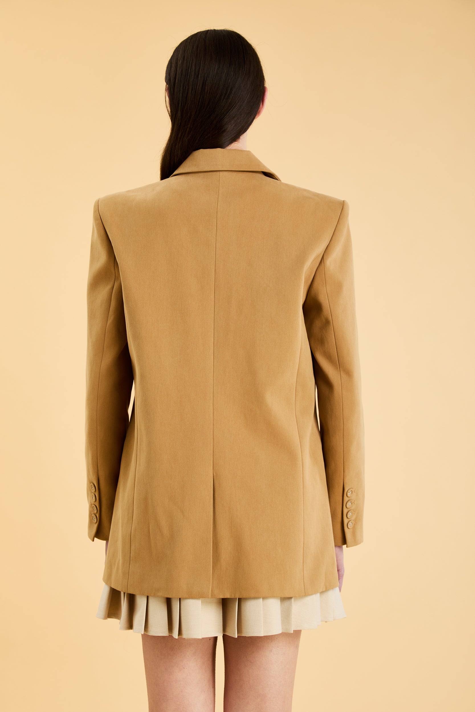 The back of a person wearing a Camel colored oversized blazer on a beige background