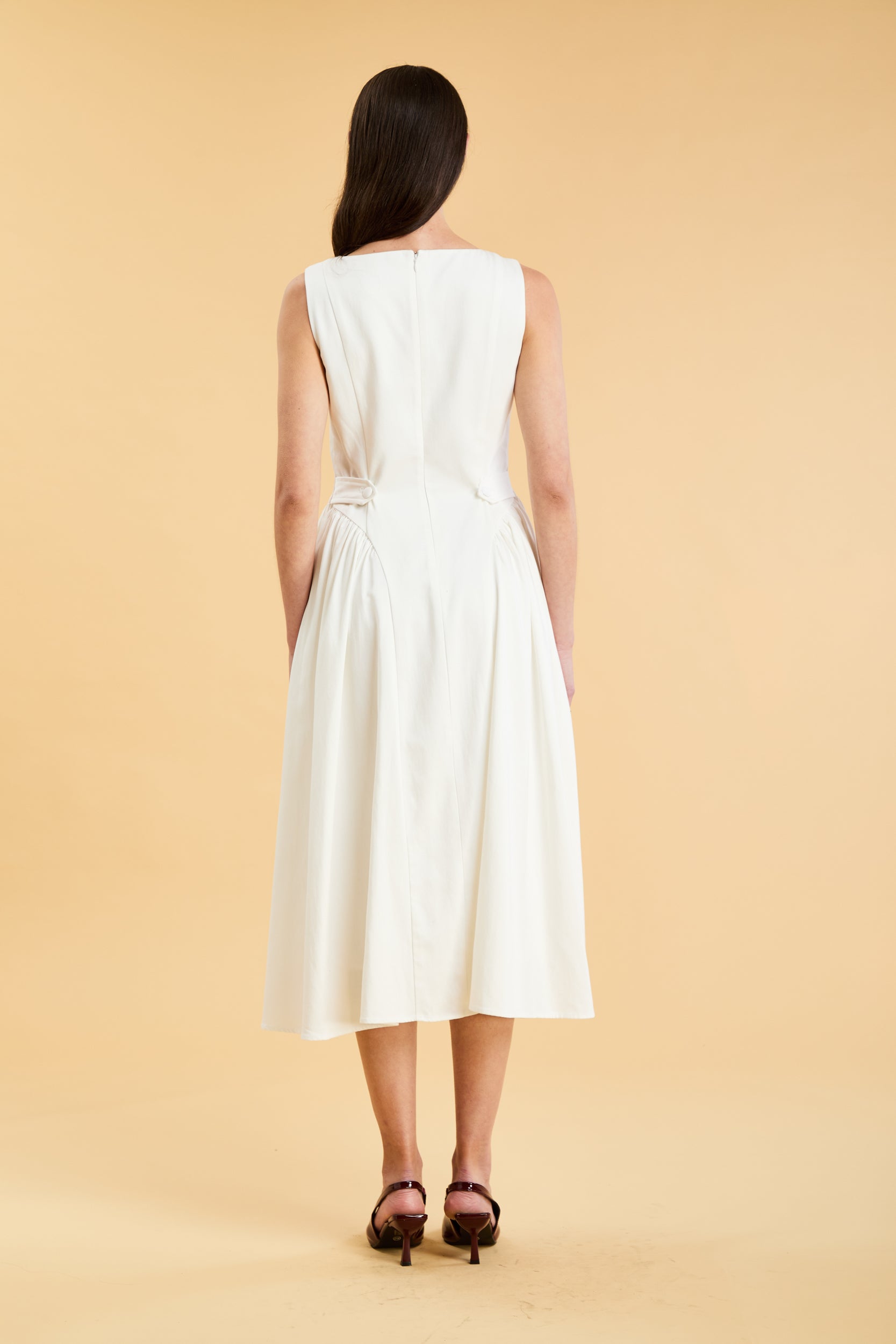 Woman wearing a Triplicity White sleeveless midi dress with gathered side panels on a beige background