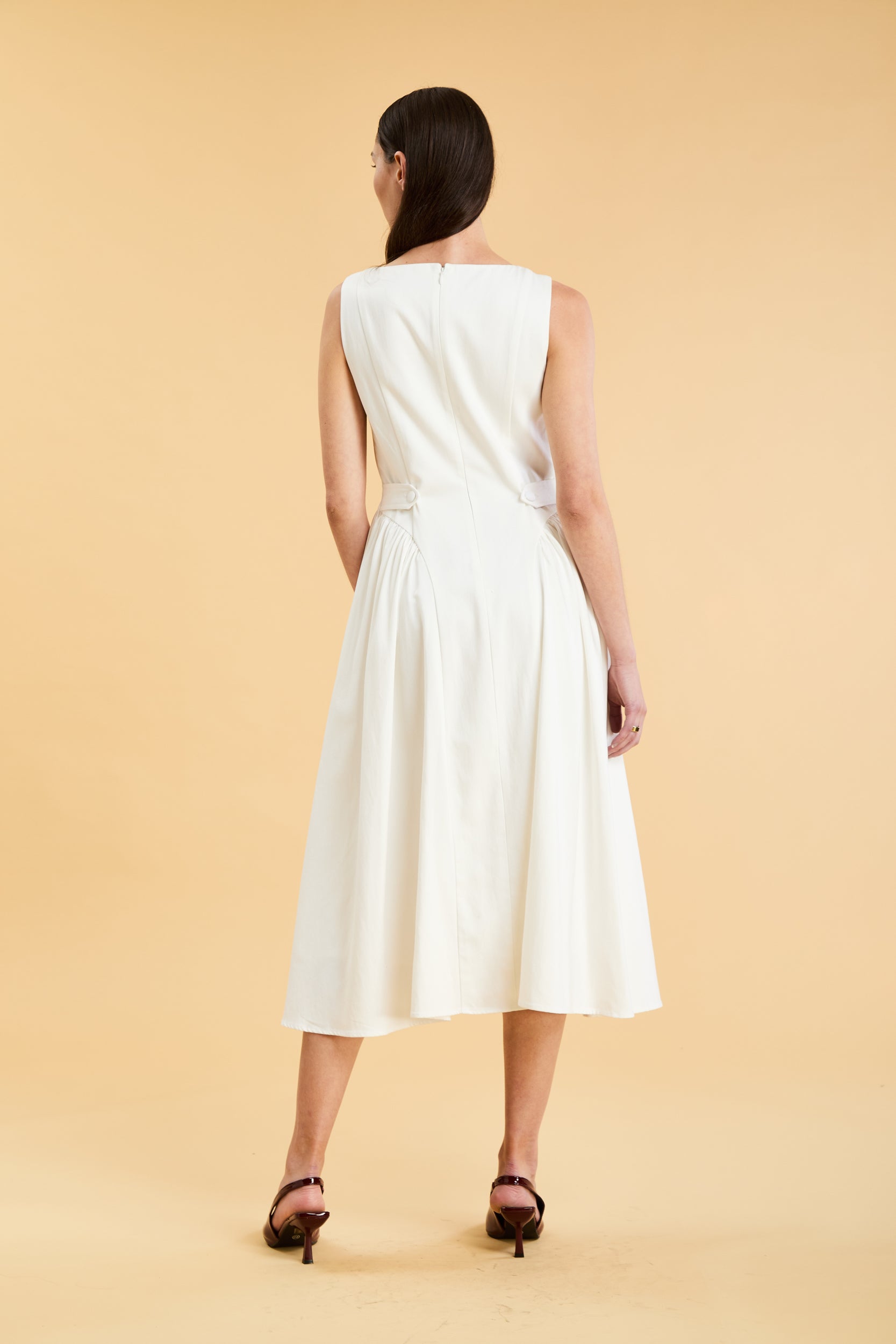 Woman wearing a Triplicity White sleeveless midi dress with gathered side panels on a beige background