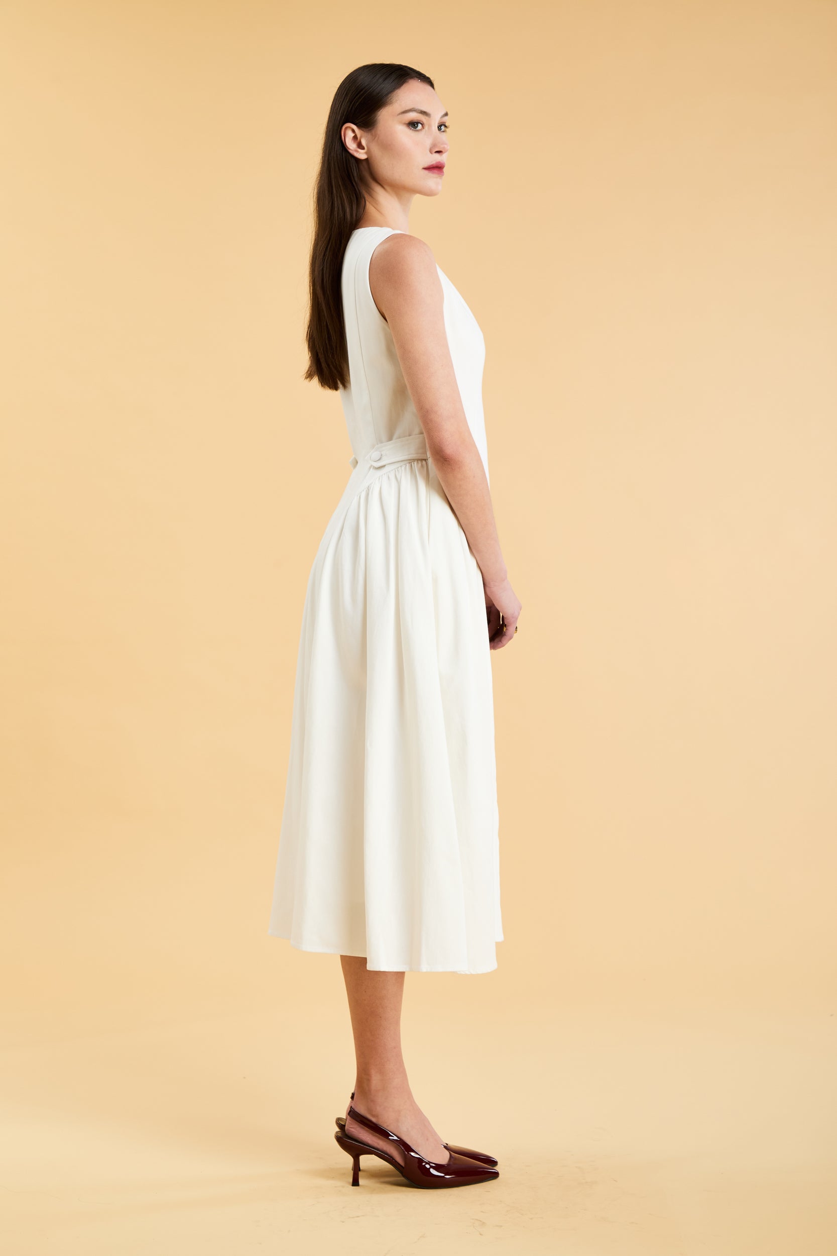 Woman wearing a Triplicity White sleeveless midi dress with gathered side panels on a beige background