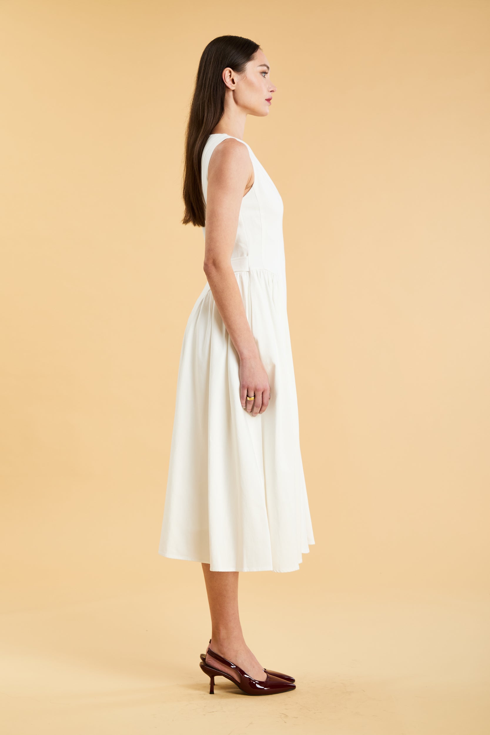 Woman wearing a Triplicity White sleeveless midi dress with gathered side panels on a beige background