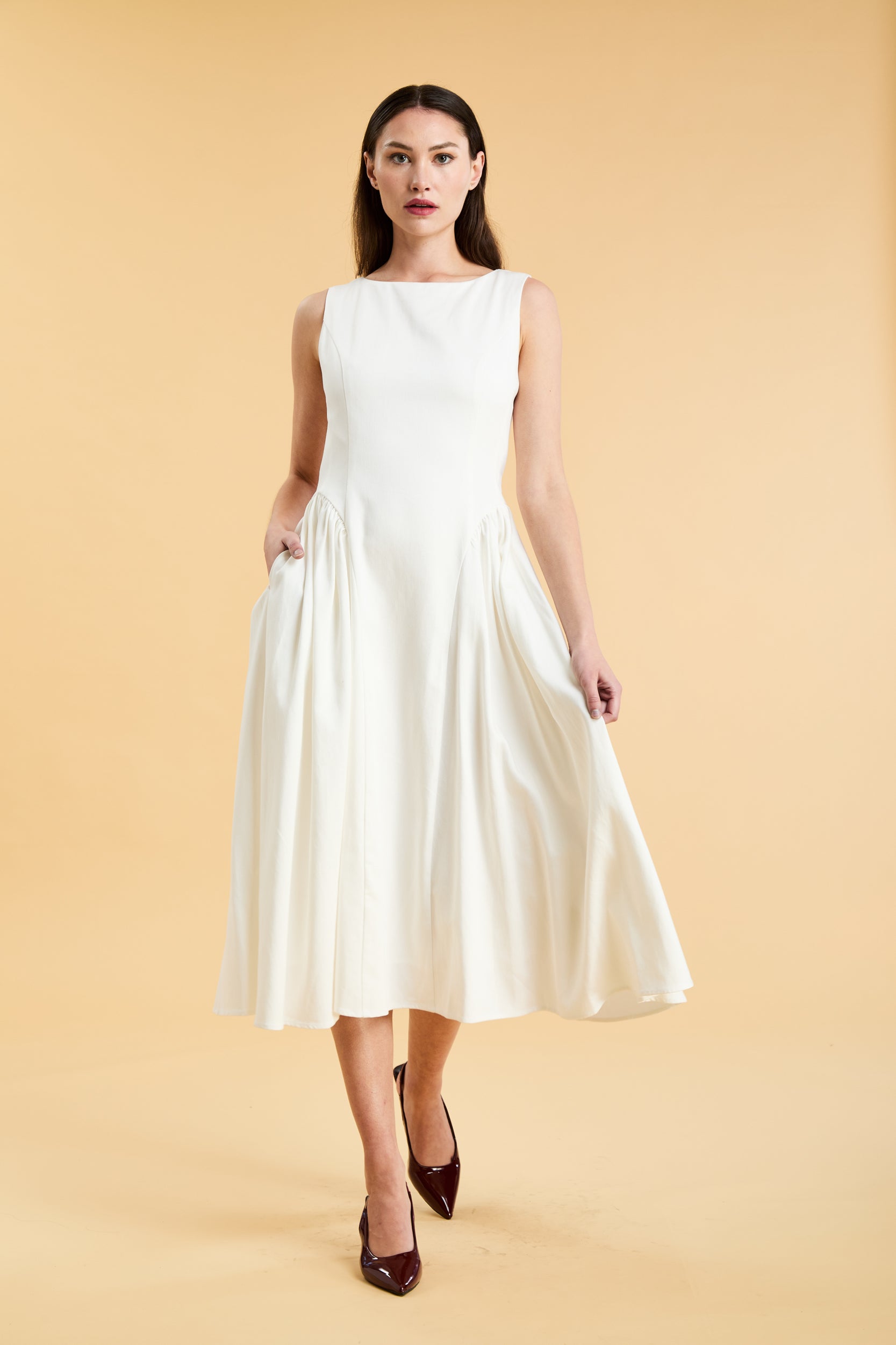 Woman wearing a Triplicity White sleeveless midi dress with gathered side panels on a beige background
