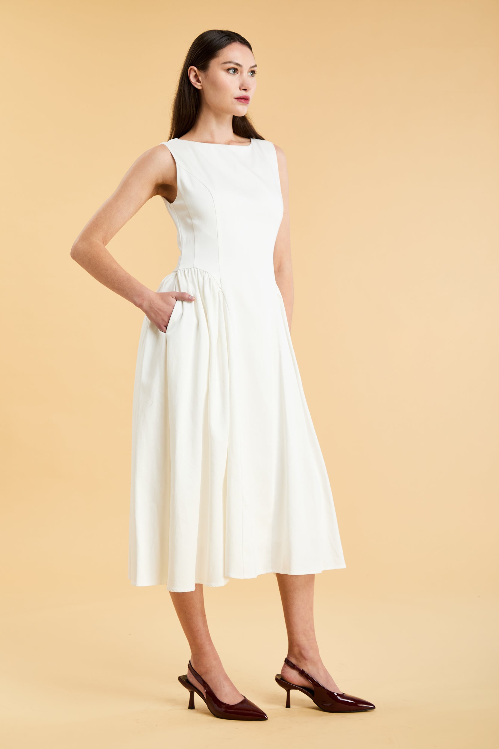 Woman wearing a Triplicity White sleeveless midi dress with gathered side panels on a beige background