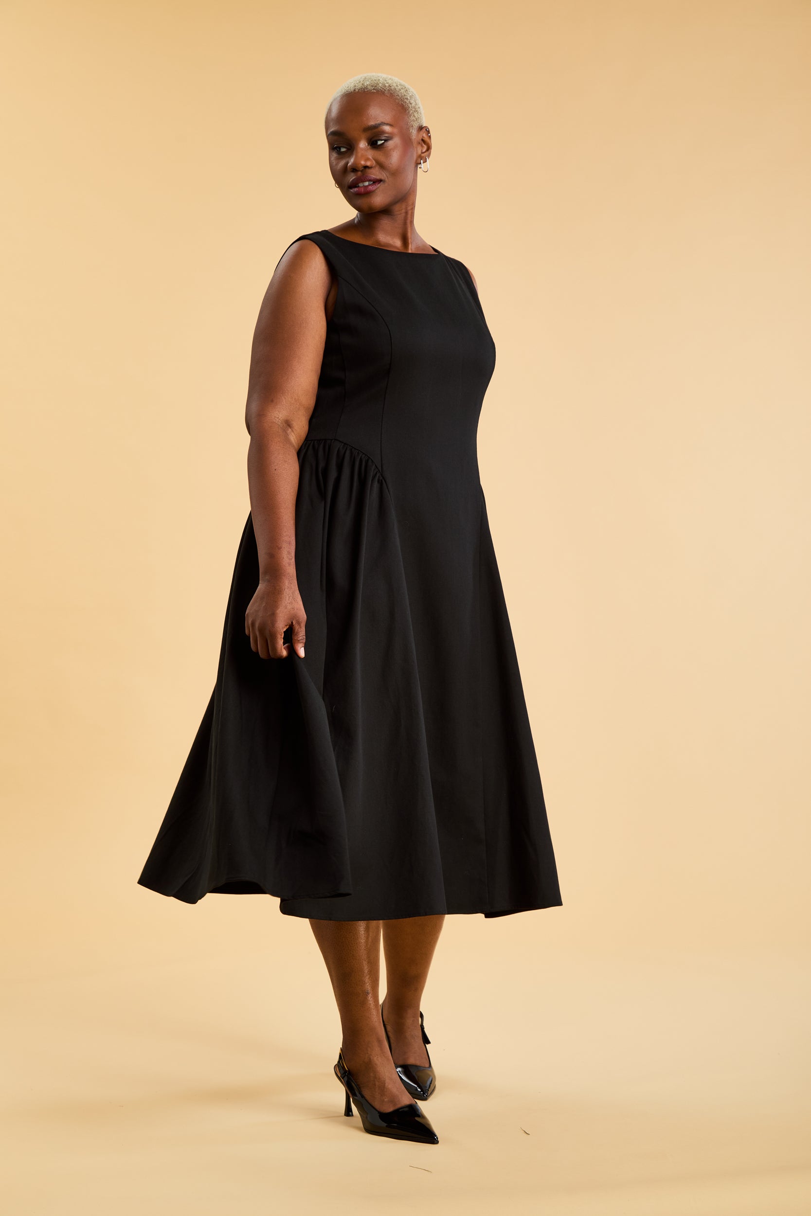 Woman wearing a Triplicity Black sleeveless midi dress with gathered side panels on a beige background