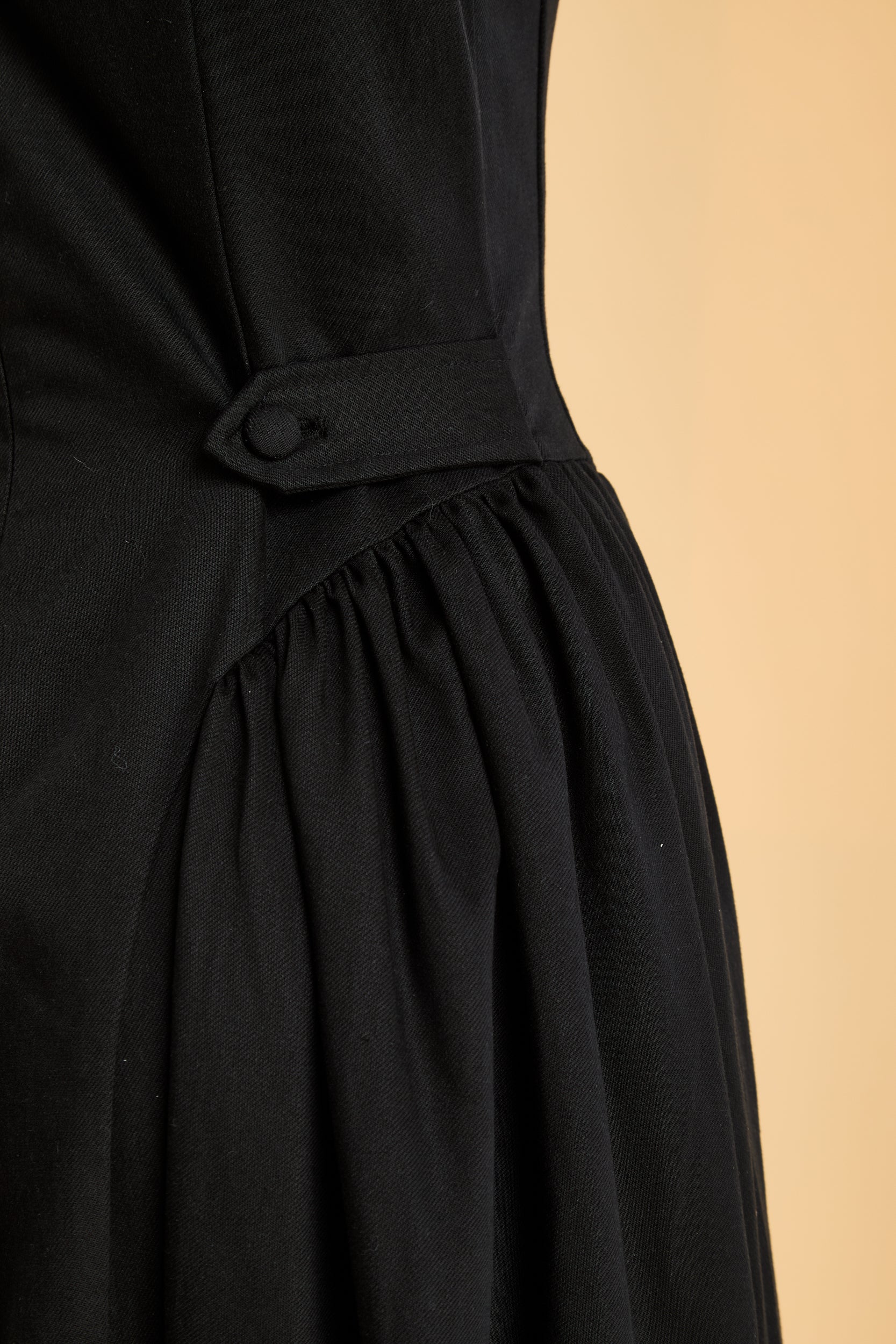 Black dress with an adjustable button detail on a beige background