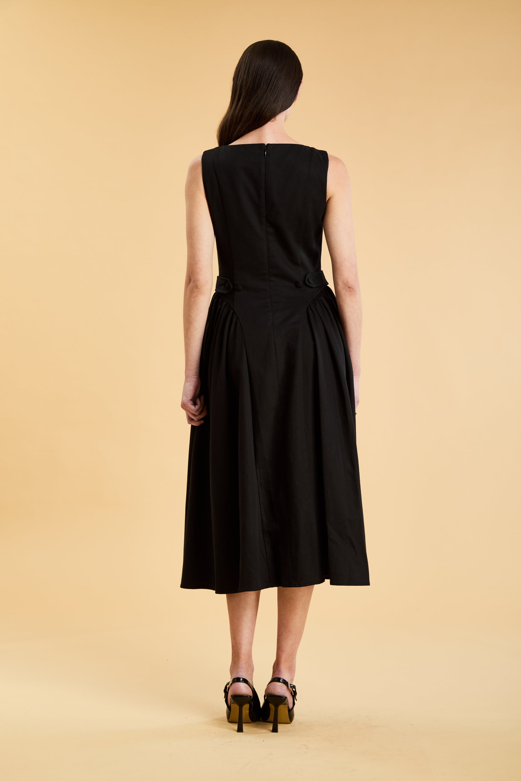 Woman wearing a Triplicity Black sleeveless midi dress with gathered side panels on a beige background