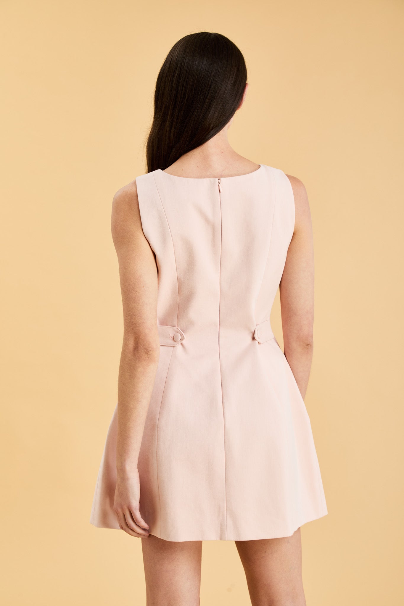 Woman wearing a blush pink sleeveless mini dress against a beige background