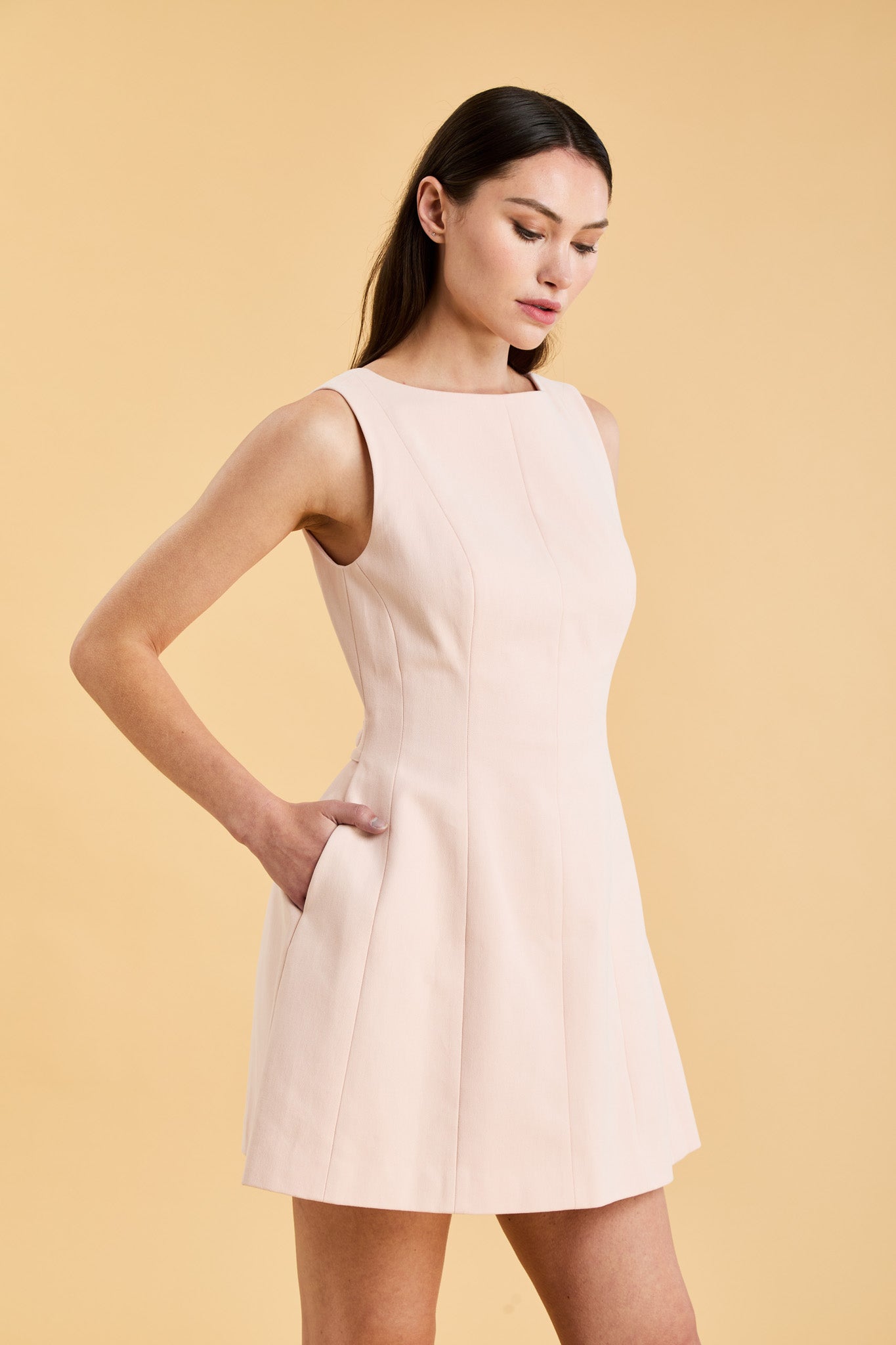 Woman wearing a blush pink sleeveless mini dress against a beige background
