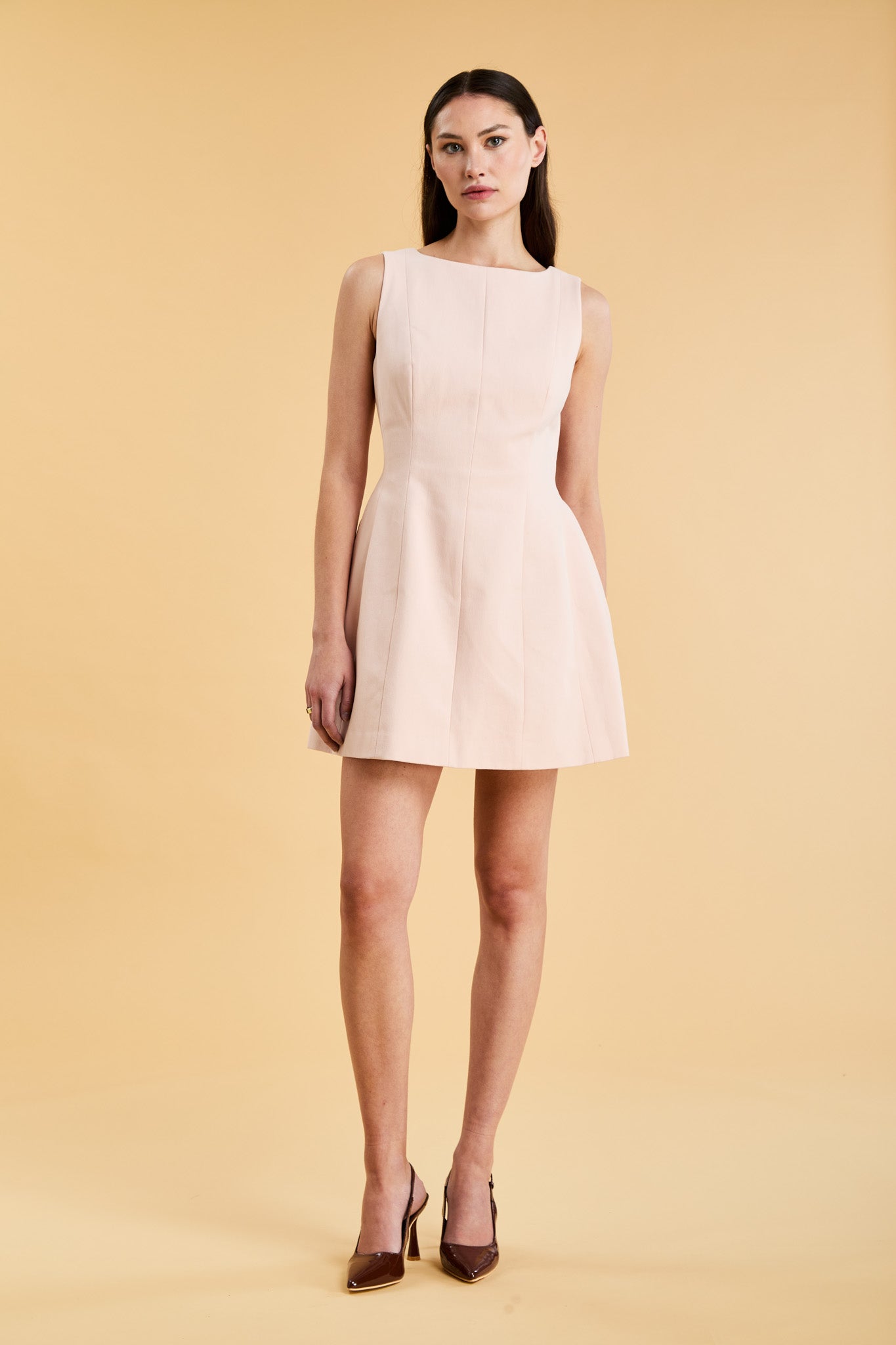 Woman wearing a blush pink sleeveless mini dress against a beige background