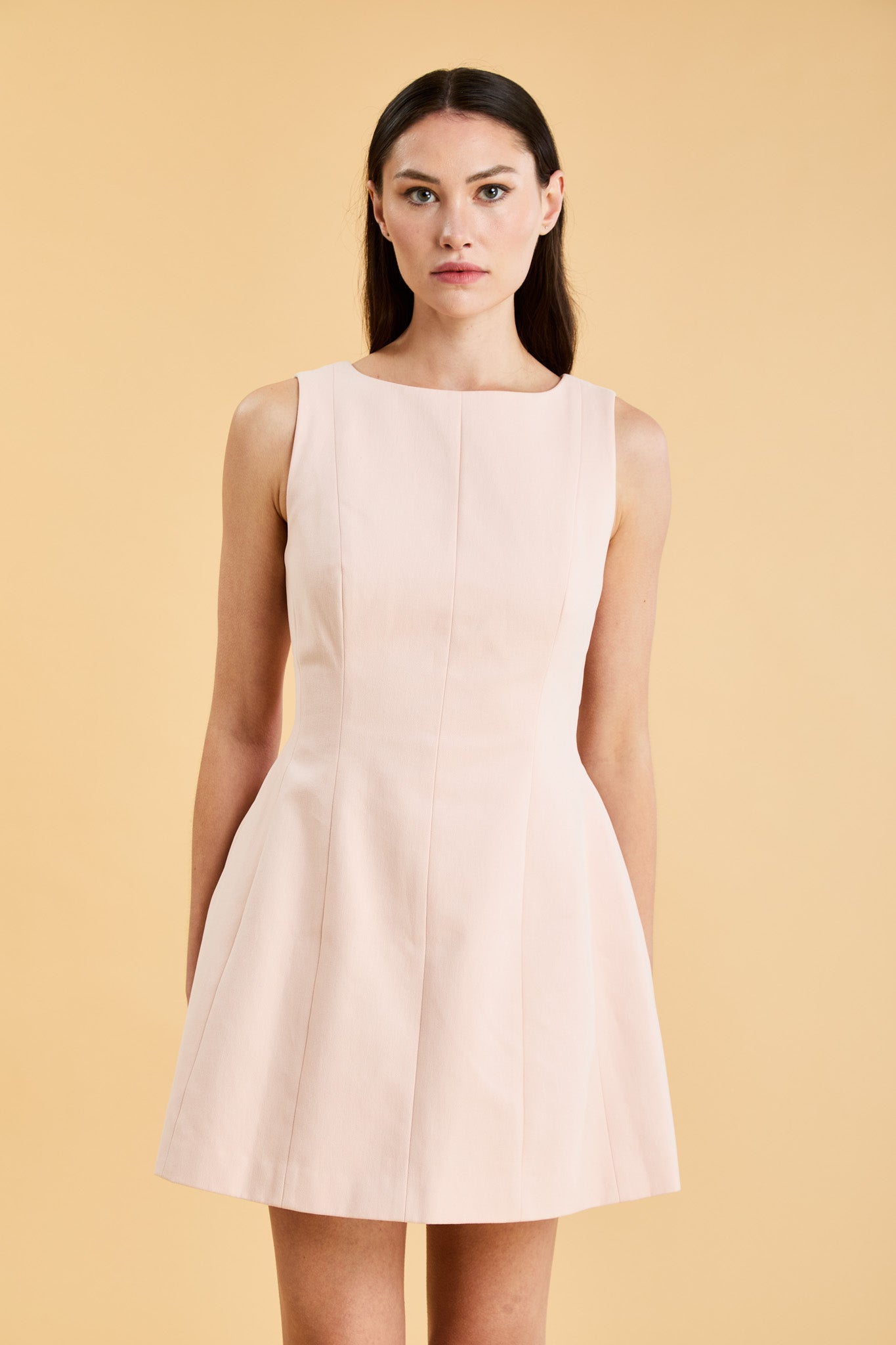 Woman wearing a blush pink sleeveless mini dress against a beige background