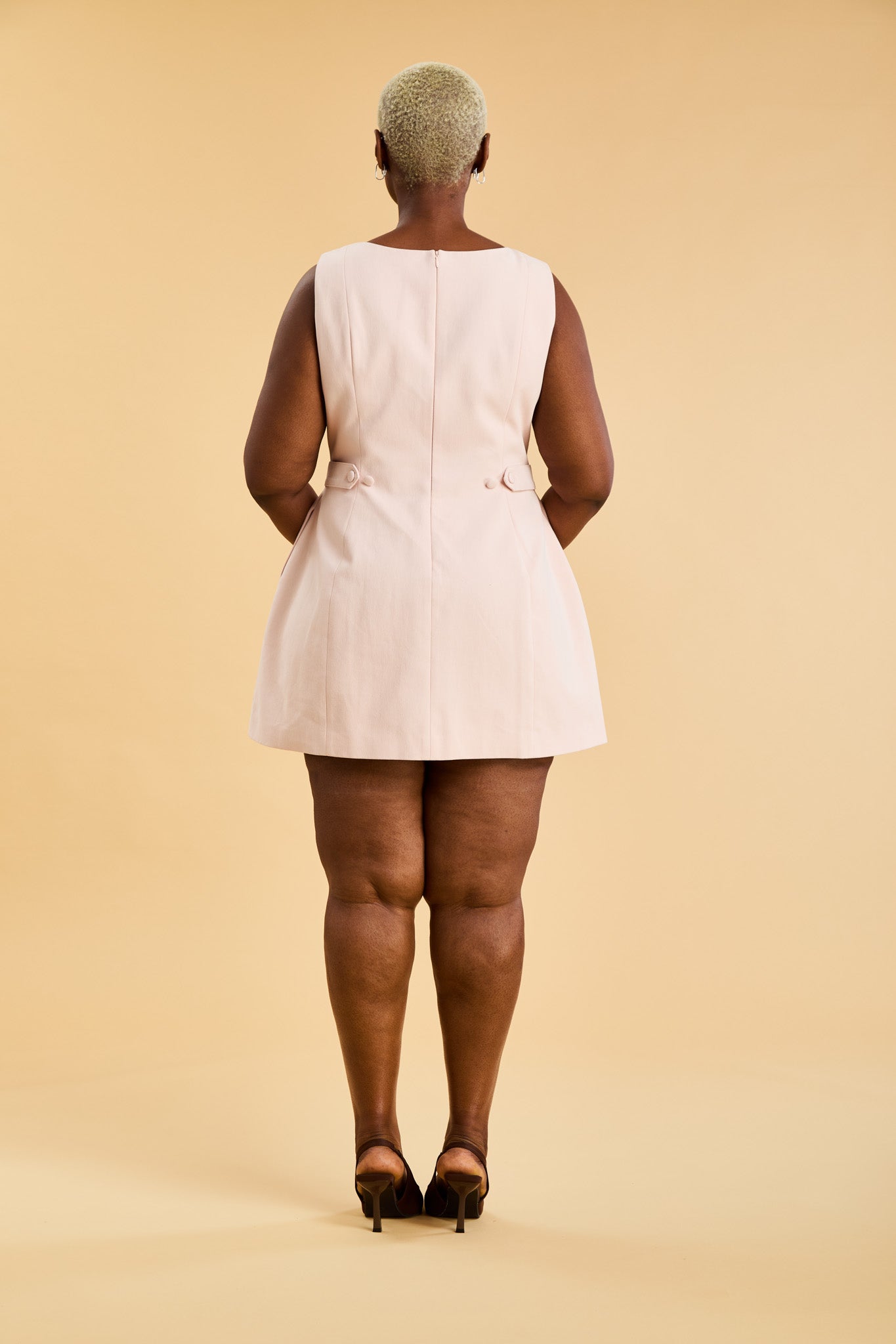 Woman wearing a blush pink sleeveless mini dress against a beige background