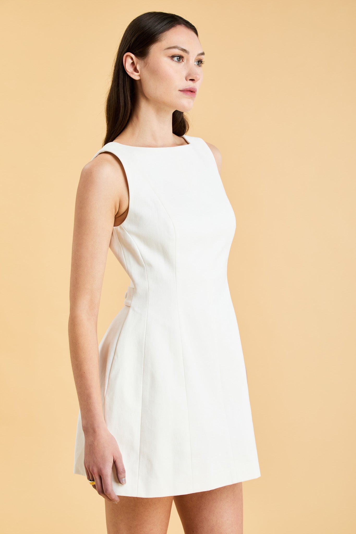 Woman wearing a white sleeveless mini dress against a beige background
