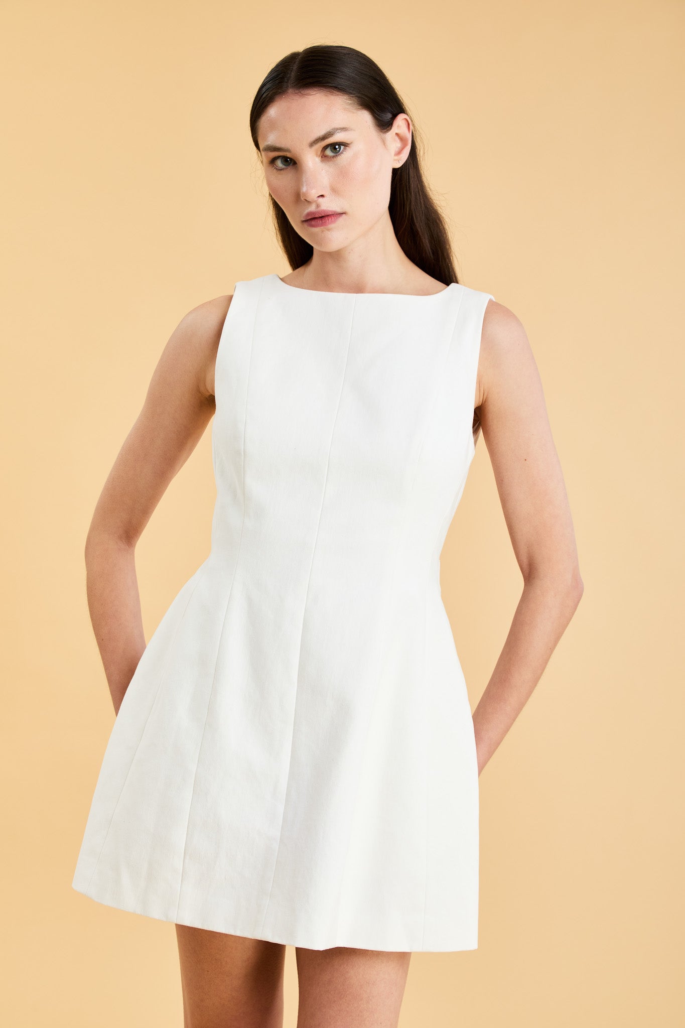 Woman wearing a white sleeveless mini dress against a beige background
