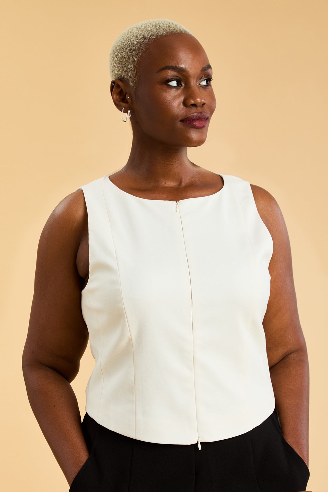 Woman wearing a white sleeveless top against a beige background