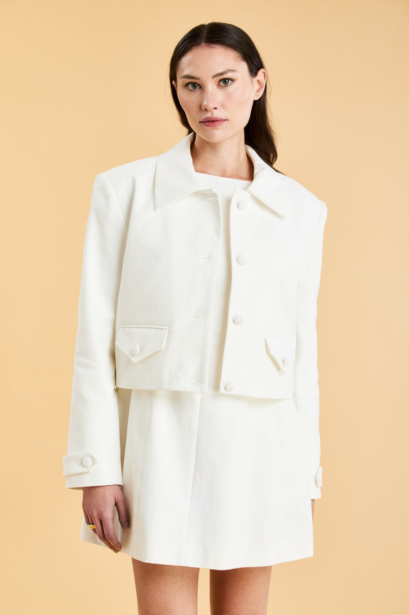 Woman wearing a White Triplicity collared tailored jacket against a beige background front view close up