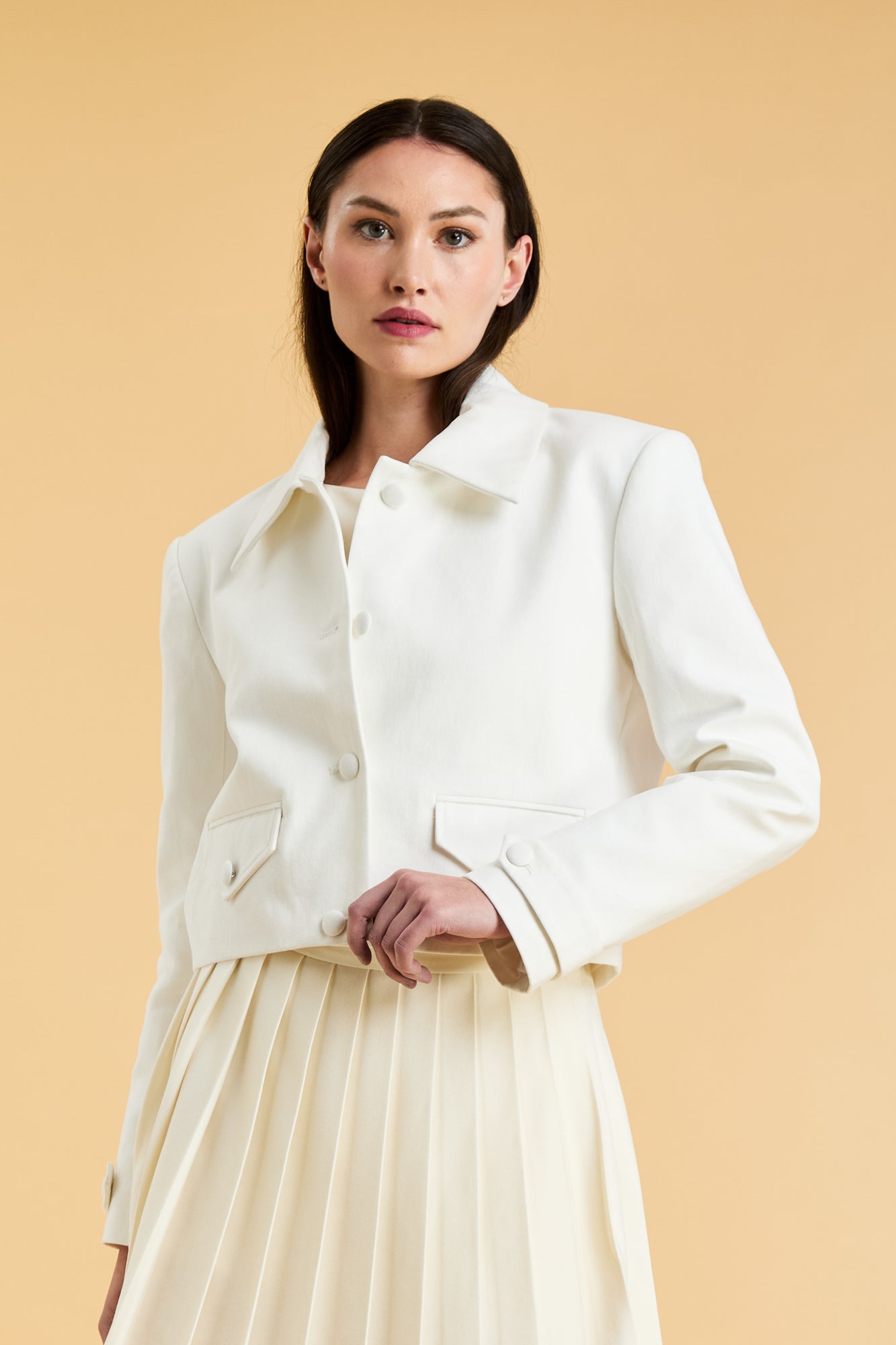Woman wearing a White Triplicity collared tailored jacket against a beige background front view close up
