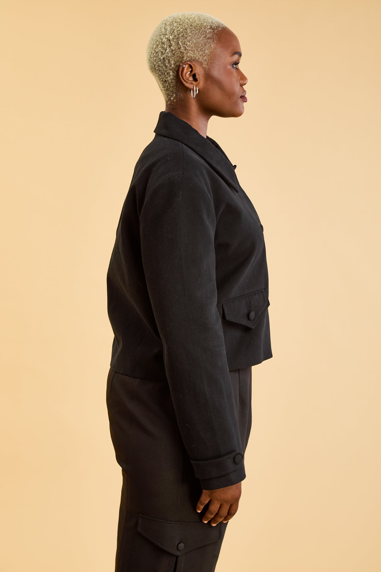 Woman wearing a Black Triplicity collared jacket and Black Triplicity pants on a beige background side close up