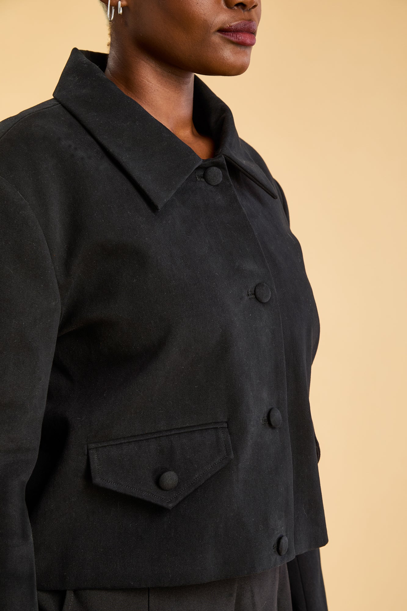 Black coat worn by a person on a beige background