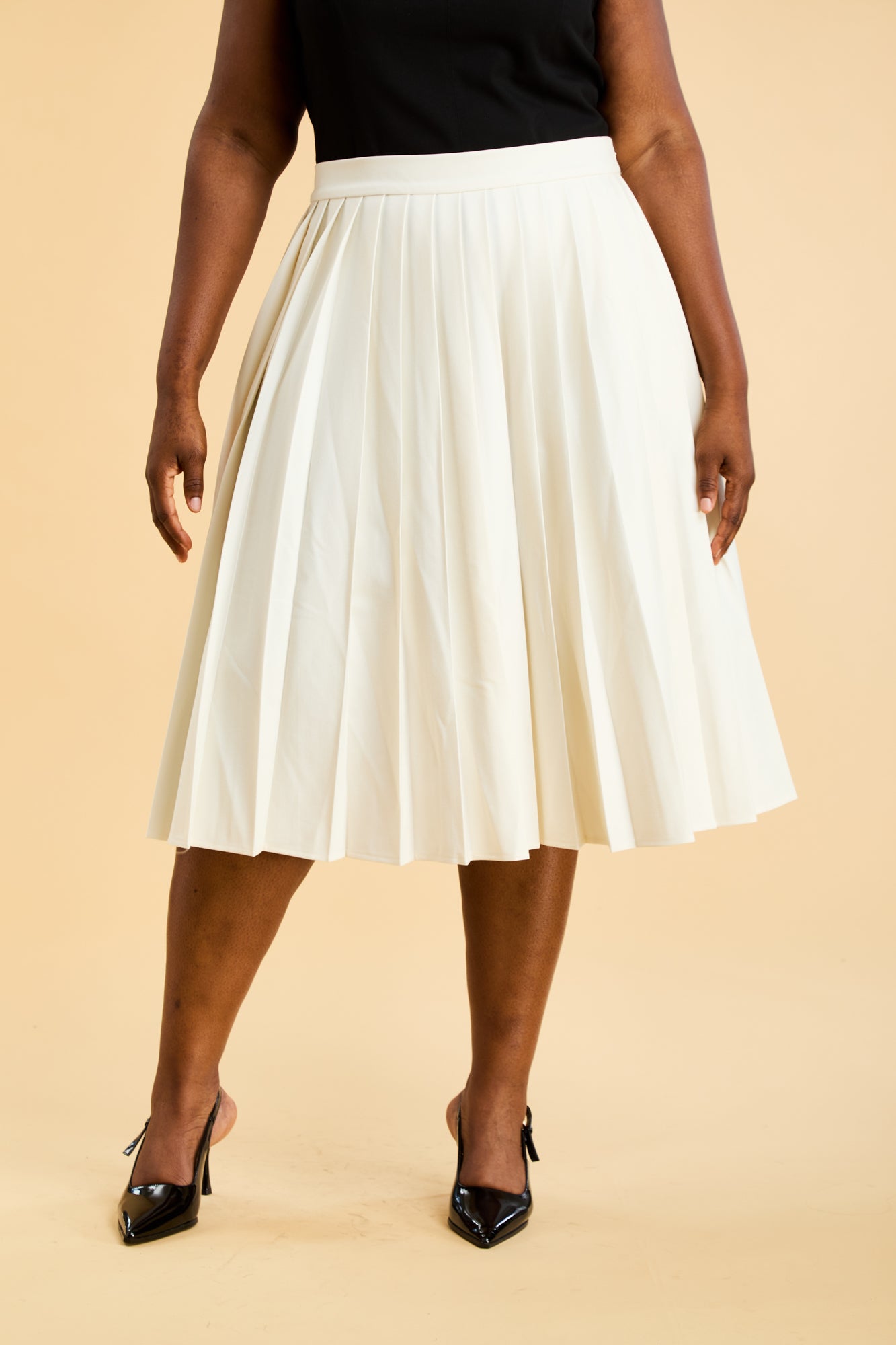 Close up of a person wearing a Triplicity White pleated skirt on a beige background close up front view