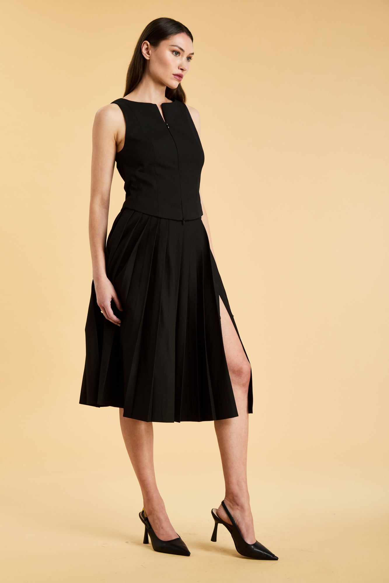 Woman wearing a black sleeveless top on a pleated Black midi skirt on a beige background