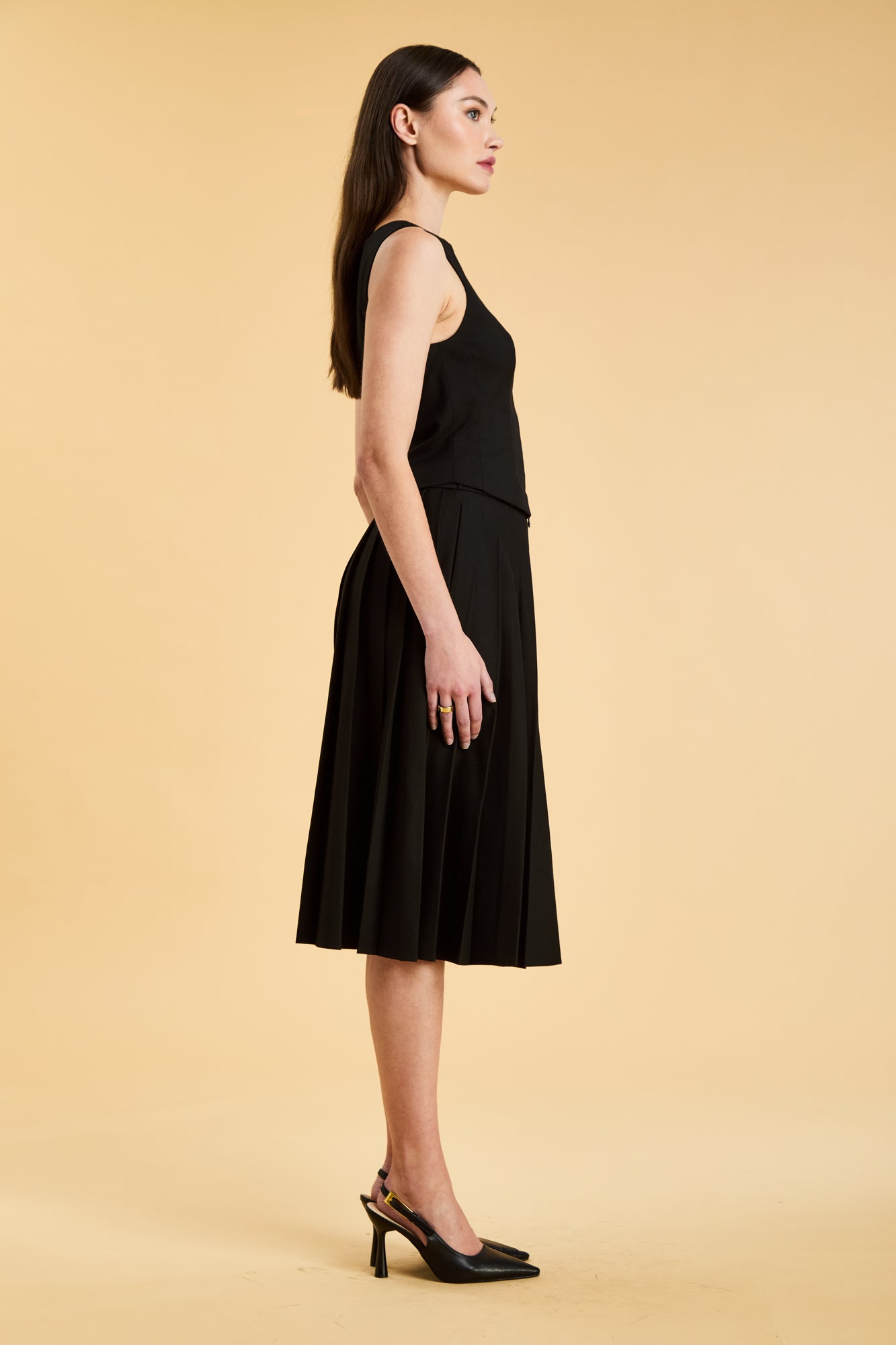 Woman wearing a black sleeveless top on a pleated Black midi skirt on a beige background