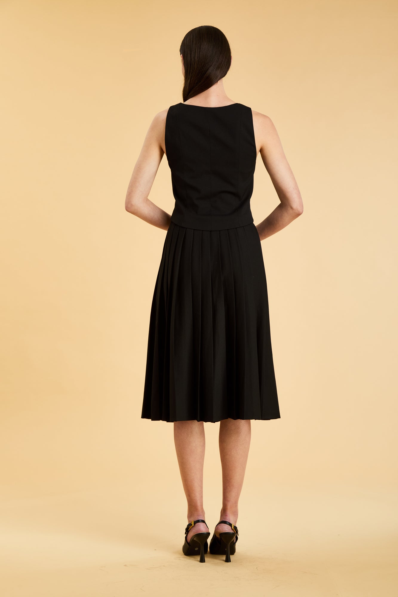 Woman wearing a black sleeveless top on a pleated Black midi skirt on a beige background