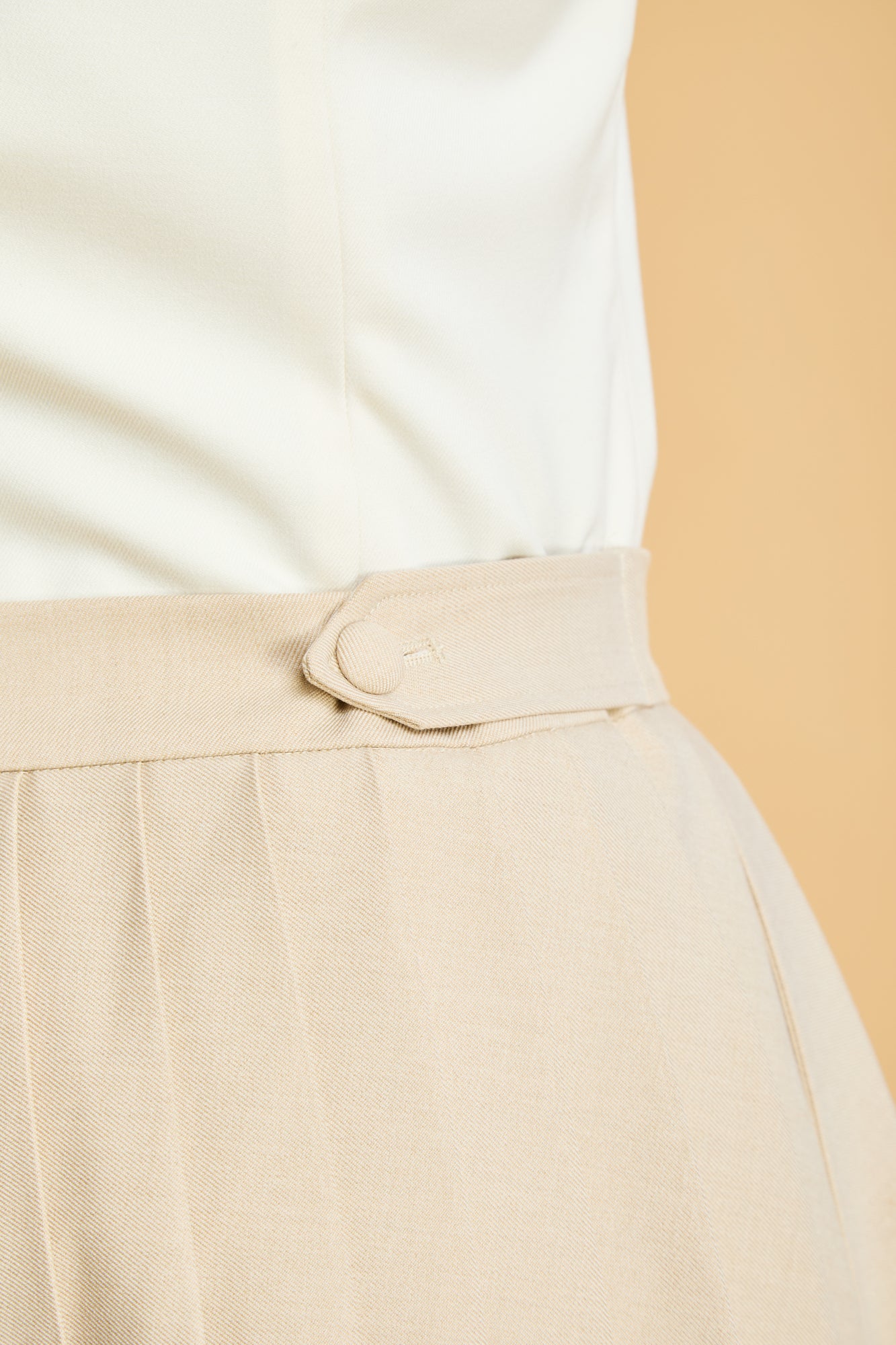 close up of the adjustable double button tab on waist of the Triplicity pleated mini skirt