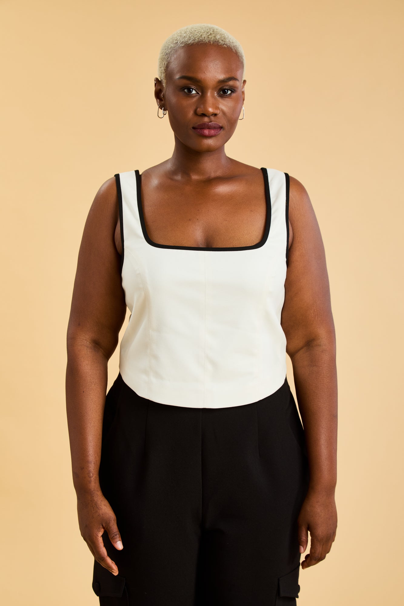 Person wearing a White Triplicity Eloise sleeveless tank top and Black Adelaide pants on a beige background front view close up