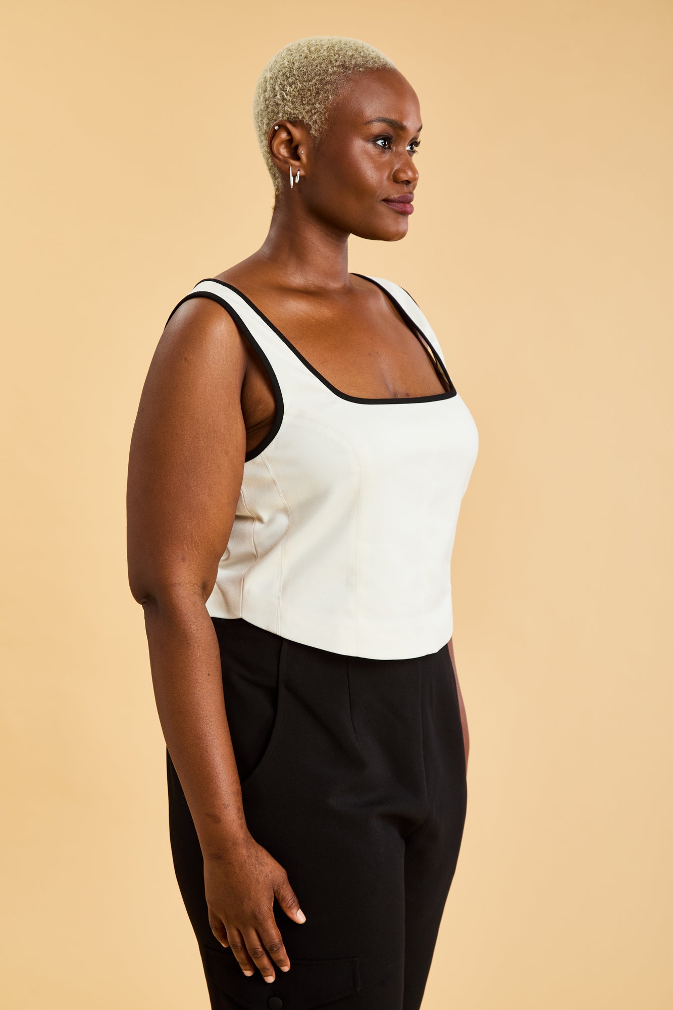 Person wearing a White Triplicity Eloise sleeveless tank top and Black Adelaide pants on a beige background three quarter view close up