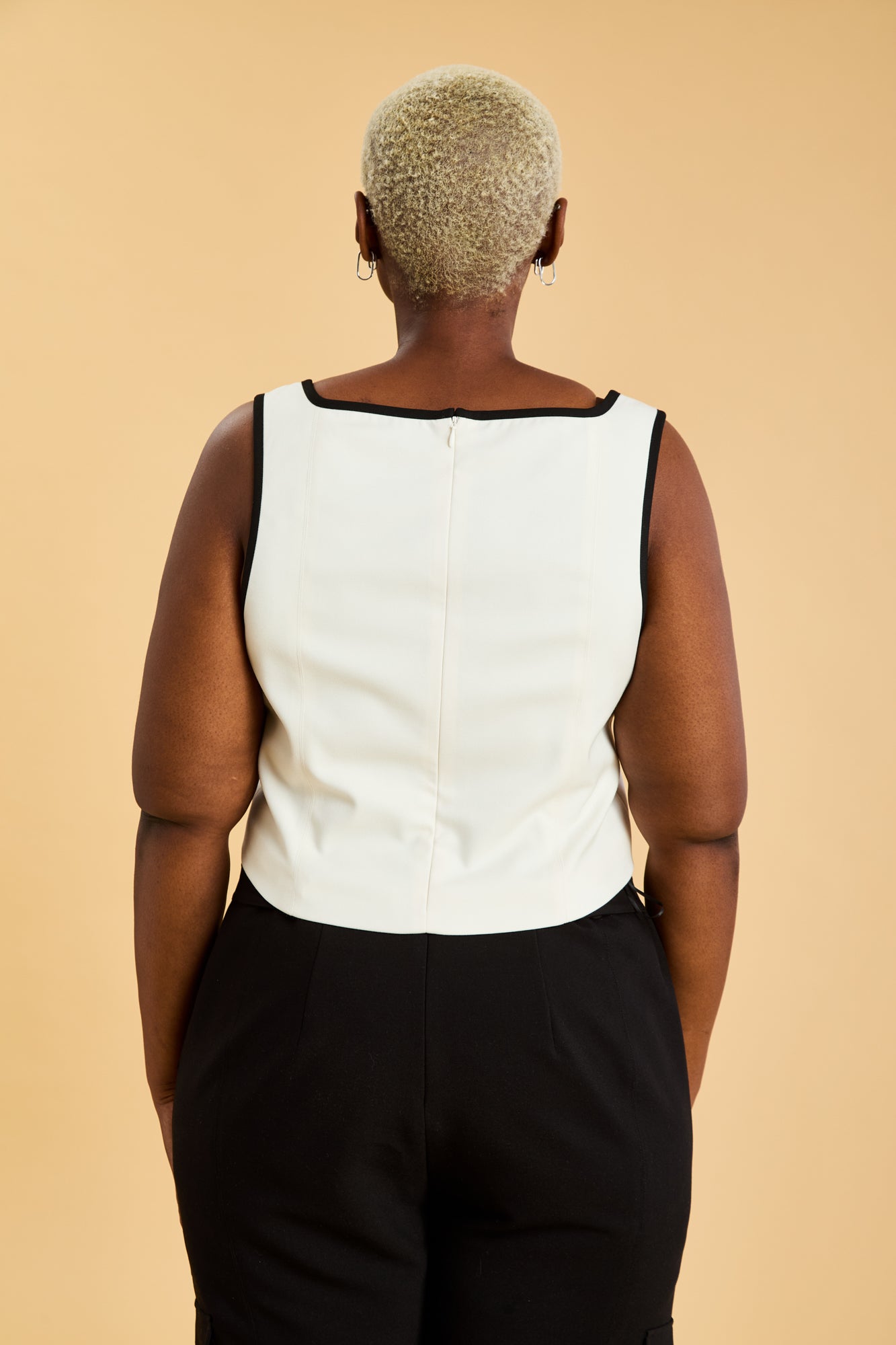 Person wearing a White Triplicity Eloise sleeveless tank top and Black Adelaide pants on a beige background back view close up