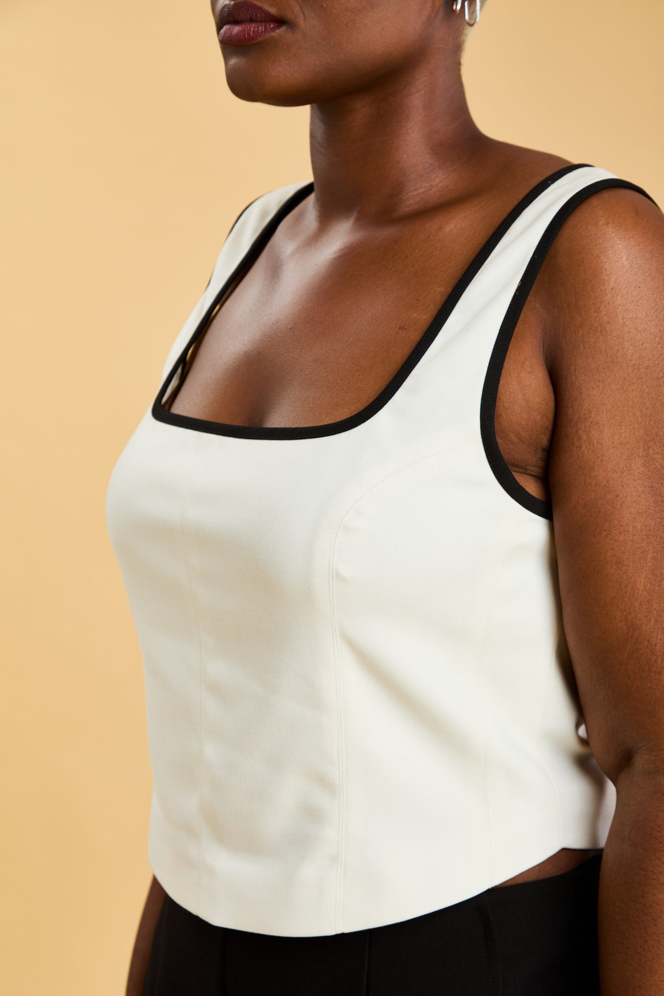 Person wearing a White Triplicity Eloise sleeveless tank top and Black Adelaide pants on a beige background three quarter view close up