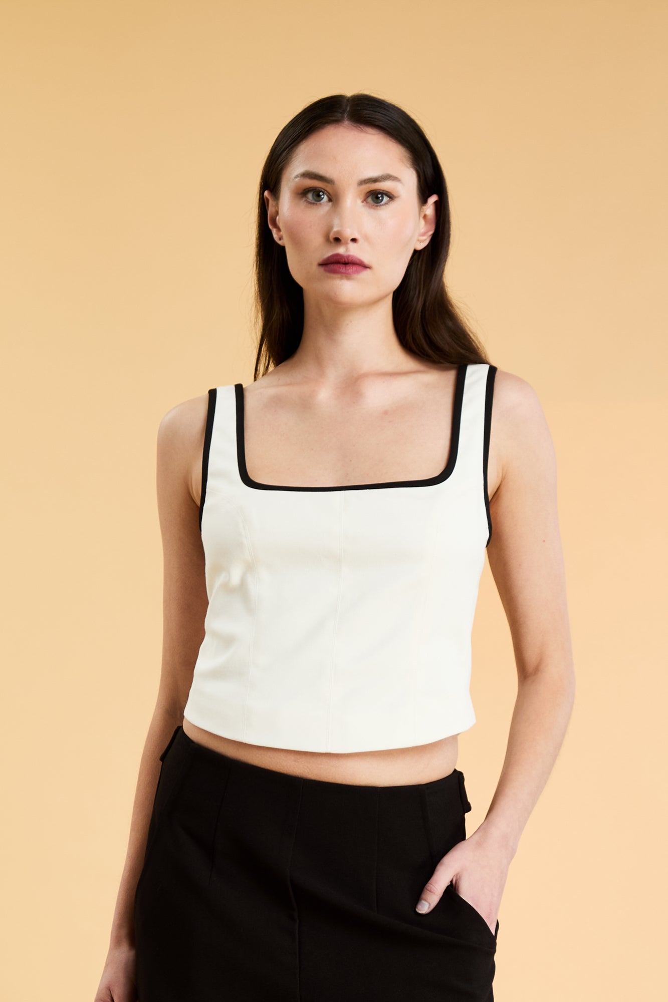 Person wearing a White Triplicity Eloise sleeveless tank top and Black Adelaide pants on a beige background front view close up