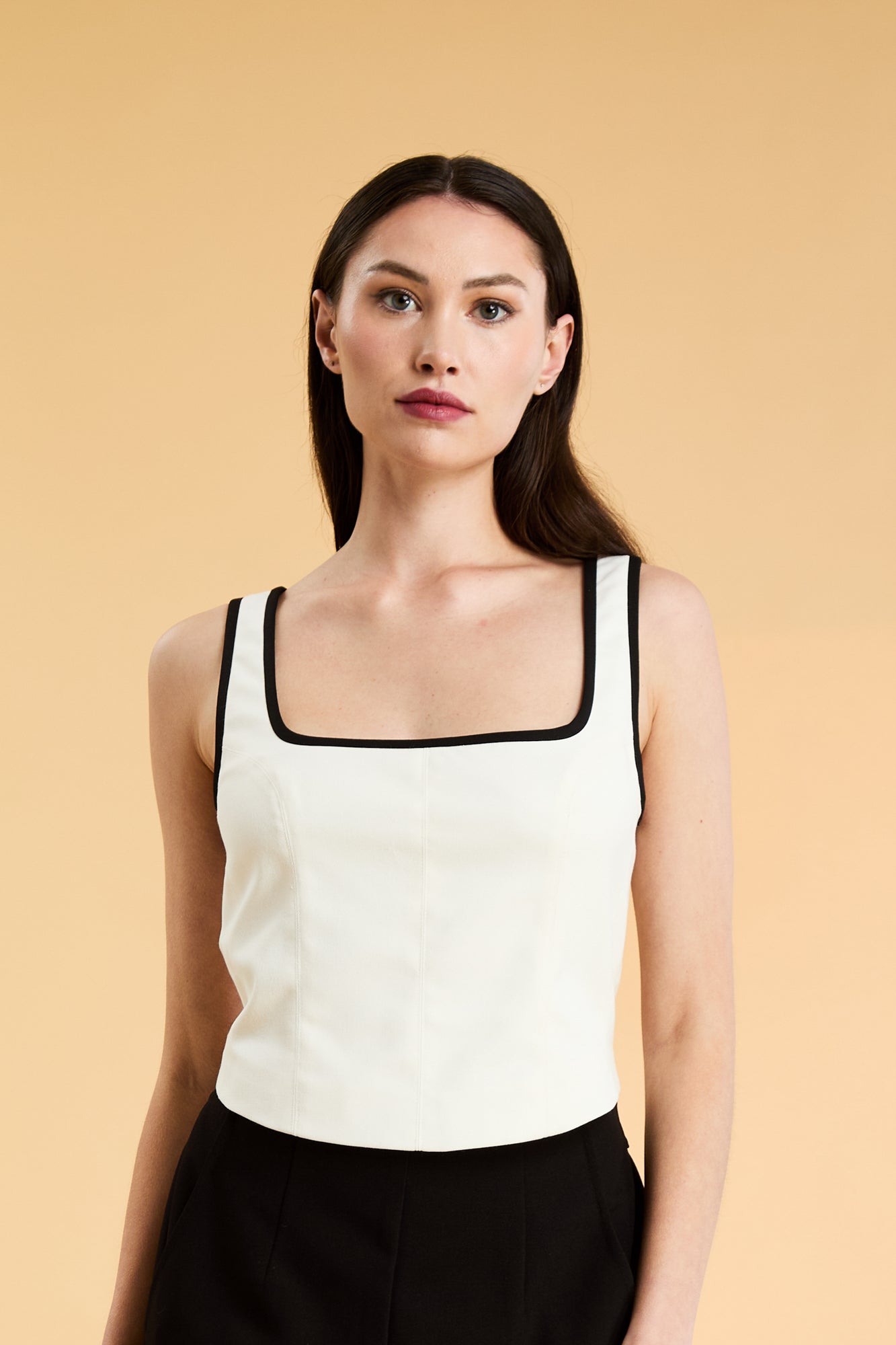Person wearing a White Triplicity Eloise sleeveless tank top and Black Adelaide pants on a beige background front view close up