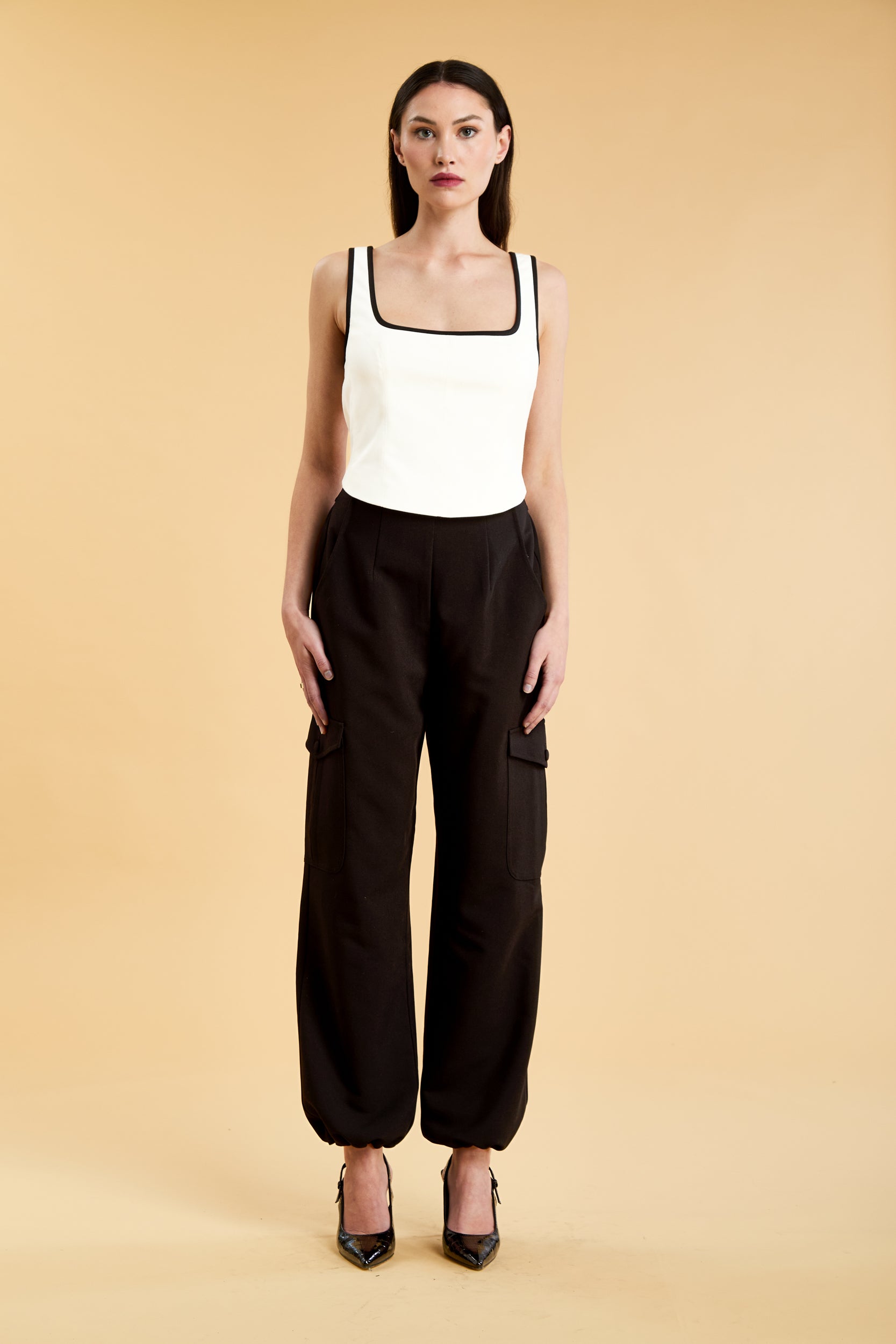 Person wearing a White Triplicity Eloise sleeveless tank top and Black Adelaide pants on a beige background front view full body