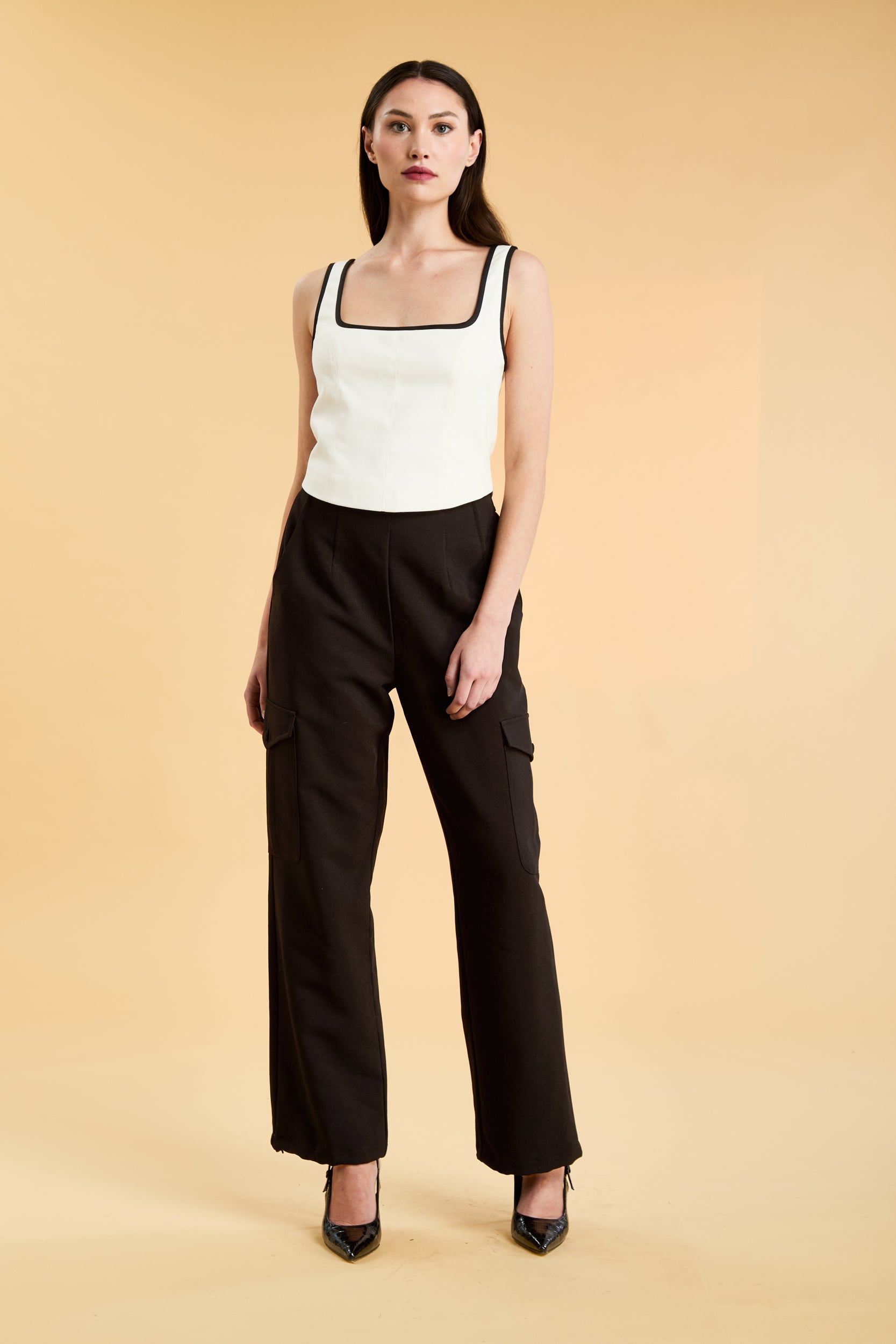 Person wearing a White Triplicity Eloise sleeveless tank top and Black Adelaide pants on a beige background front view full body